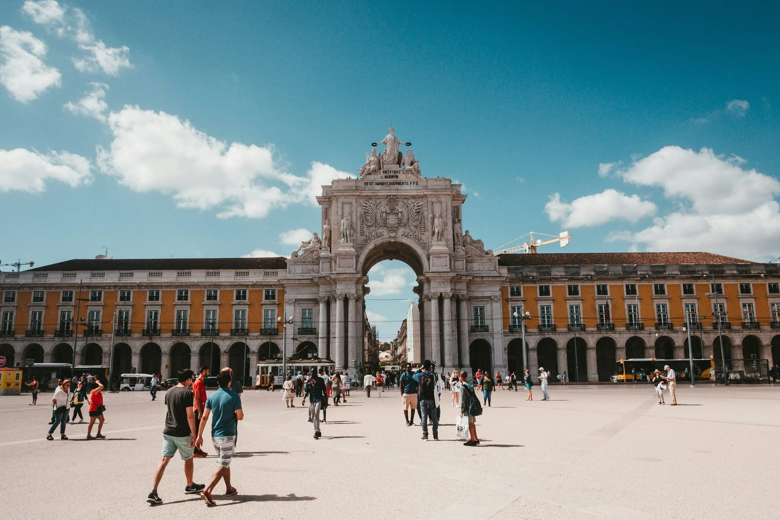 The Rua Augusta Arch across the wide paved expanse of Praca do Comercio, people crossing in ones and twos under a bright sky