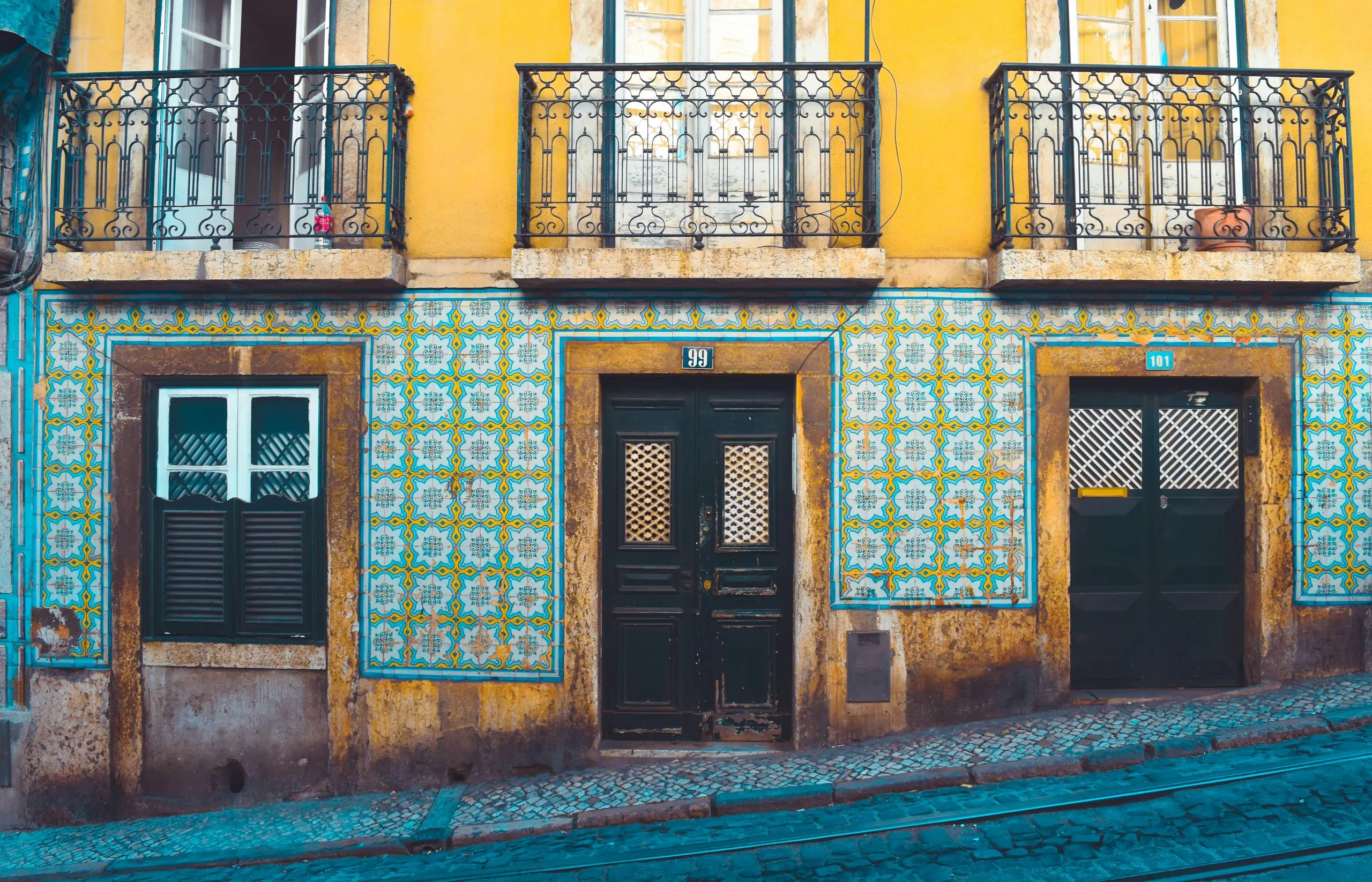 A corner building faced in green and white patterned tiles below a yellow upper storey with wrought-iron balconies