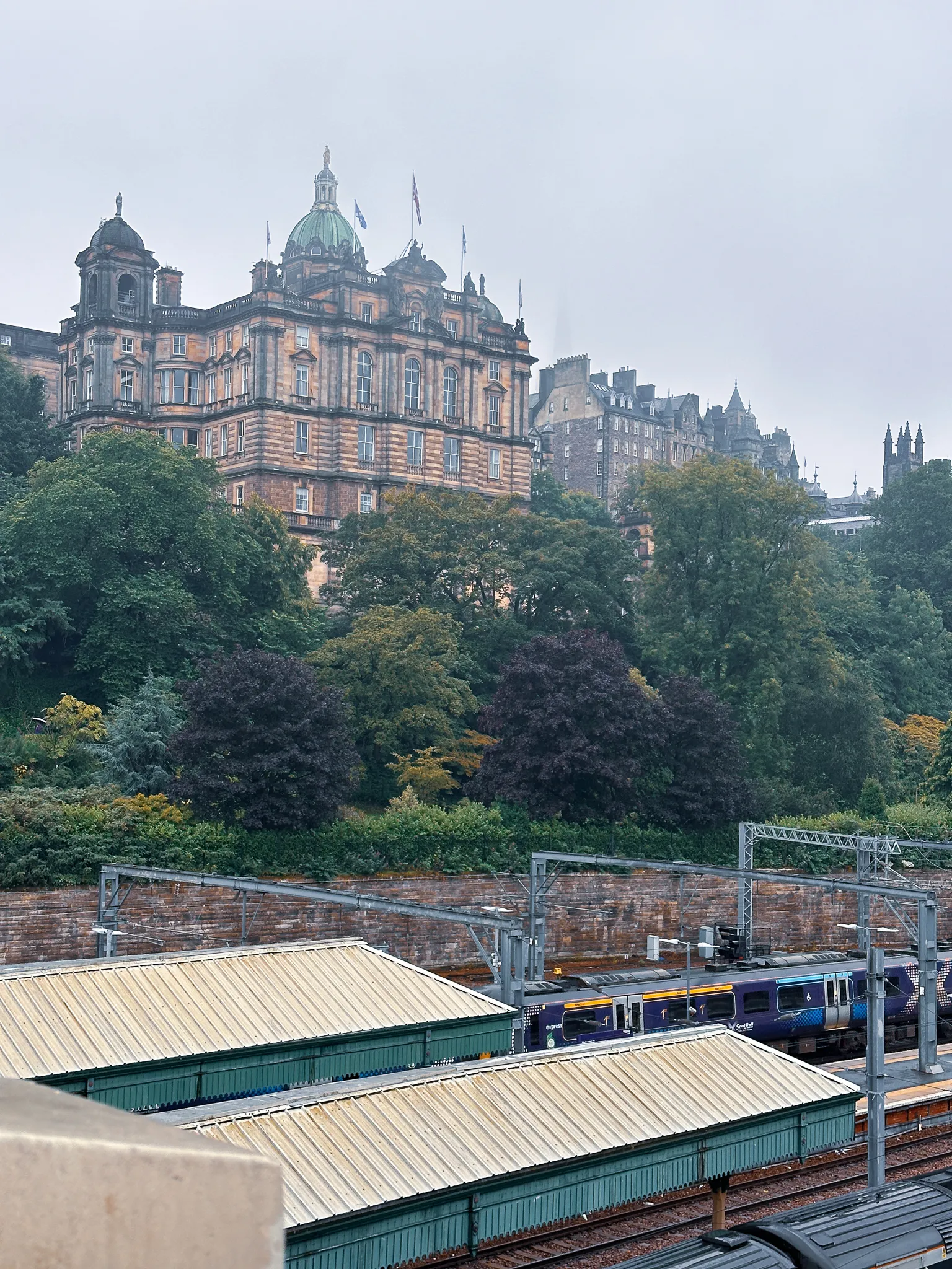 The Bank of Scotland's green dome above the trees on the Mound, a blue ScotRail train waiting under the ribbed roofs of Waverley's platforms