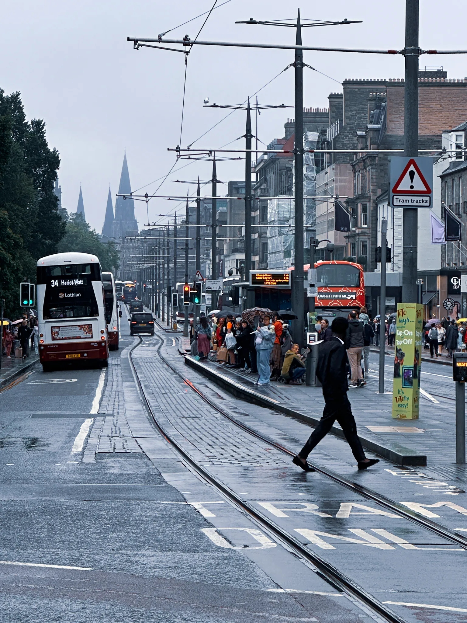 Princes Street in the rain - tram tracks curving past a crowded stop, a Lothian double-decker pulling away and spires dissolving down the far end