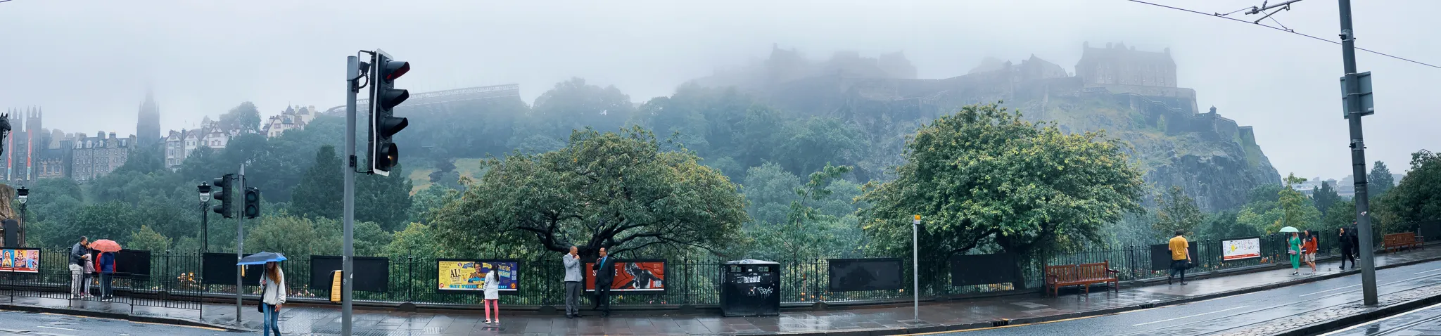 A panorama from Princes Street, the castle rock swallowed almost whole by low cloud above the gardens and umbrellas waiting at the crossing
