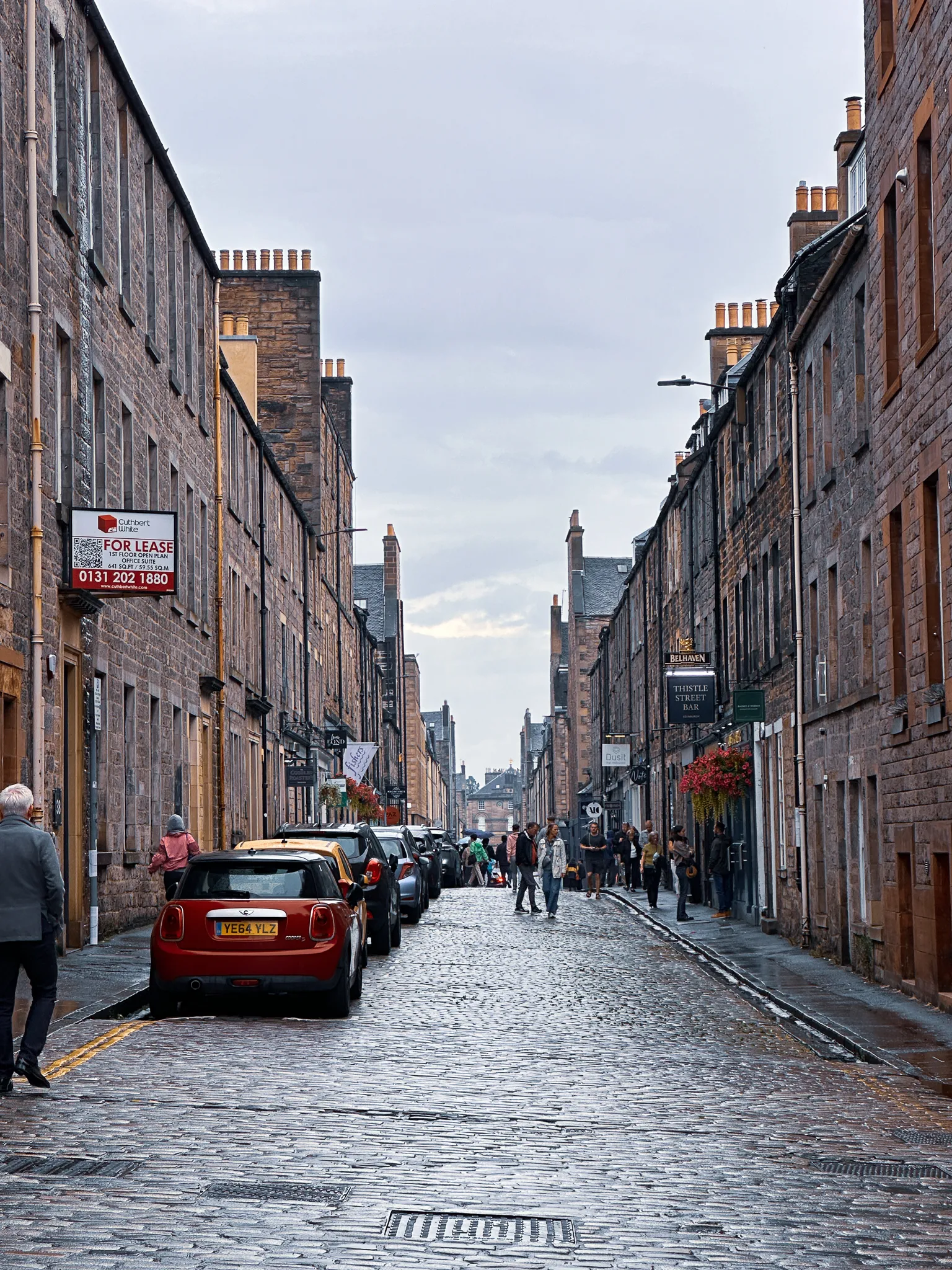 Thistle Street in the wet - a red Mini on the cobbles, hanging baskets out and the Thistle Street Bar's sign down the narrow lane