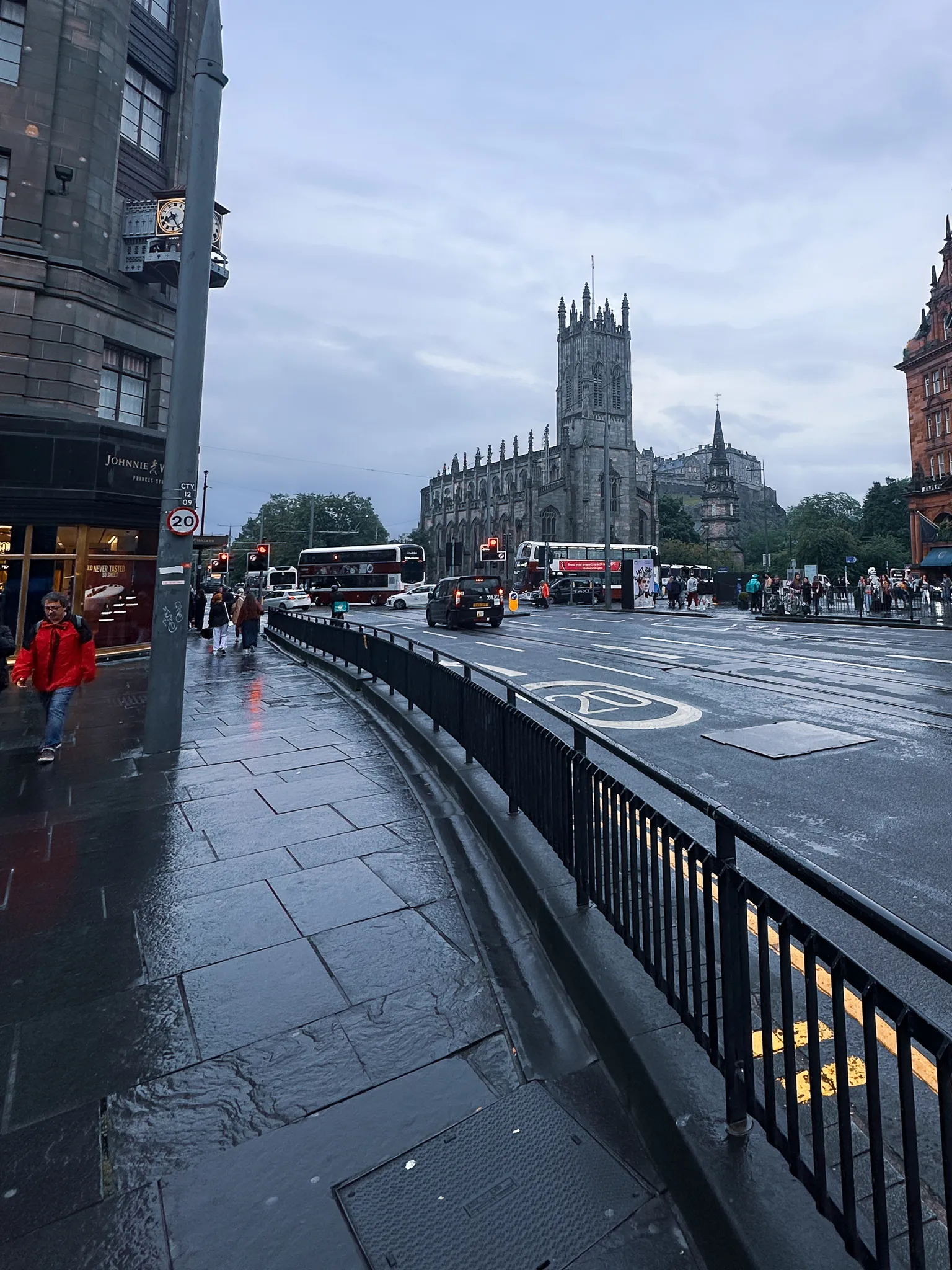 The same corner from under the Johnnie Walker clock - wet flagstones, a curve of black railings and St John's tower against the evening grey