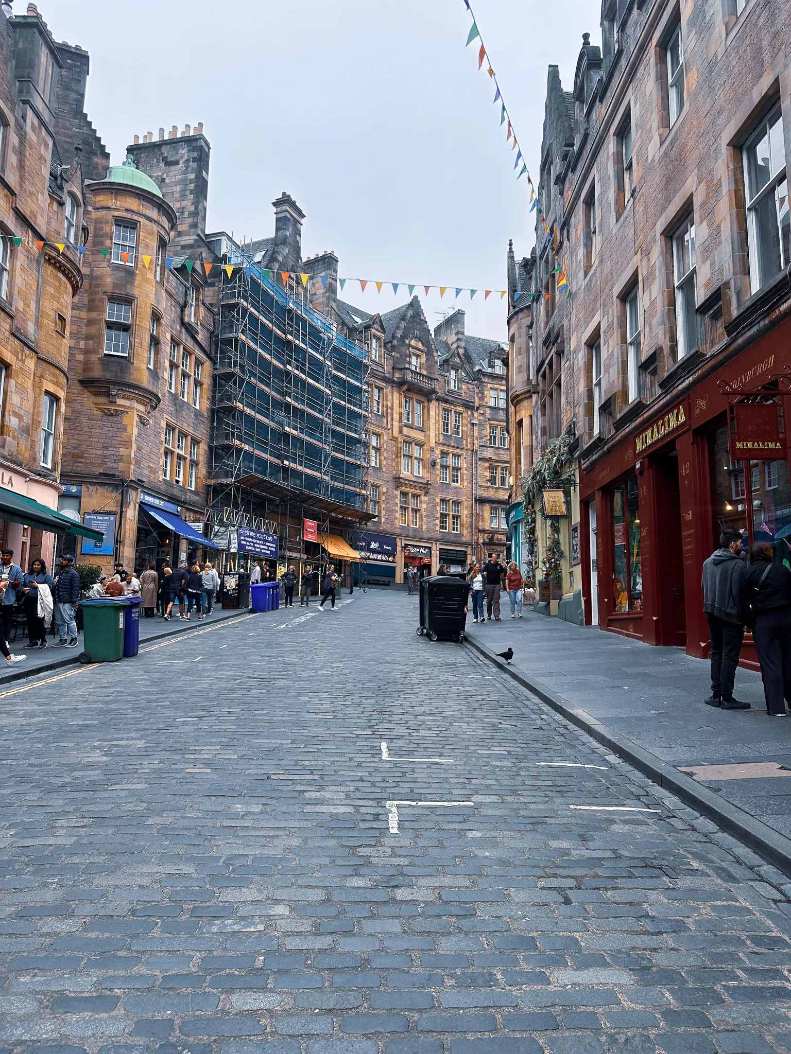 Bunting strung over the West Bow, scaffolding wrapping one tenement and the dark red front of MinaLima at the corner of Victoria Street