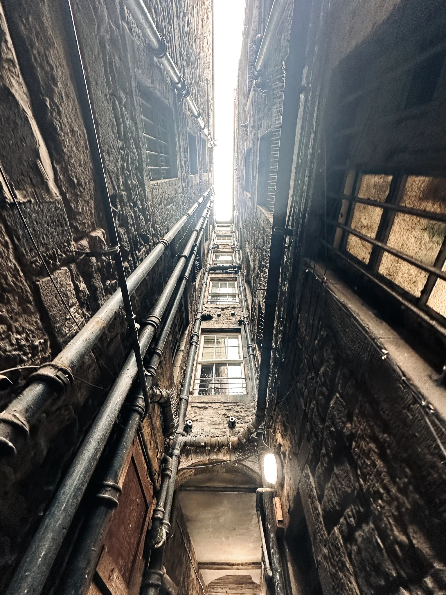 Straight up in a close - a slot of white sky between two tenements, downpipes stitched to the stone the whole way down
