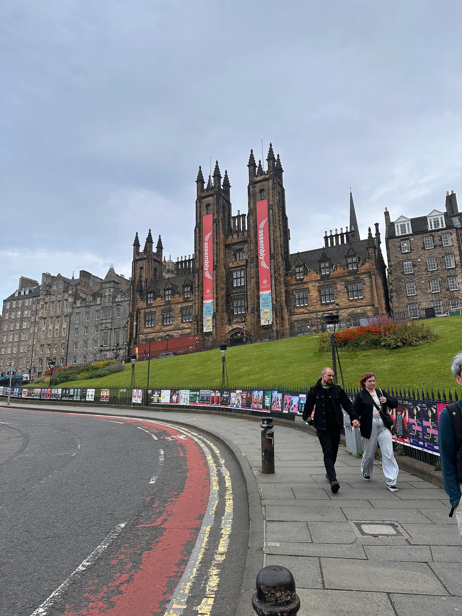 The Assembly Hall's towers on the Mound wearing red festival banners, the railings below already papered with Fringe posters