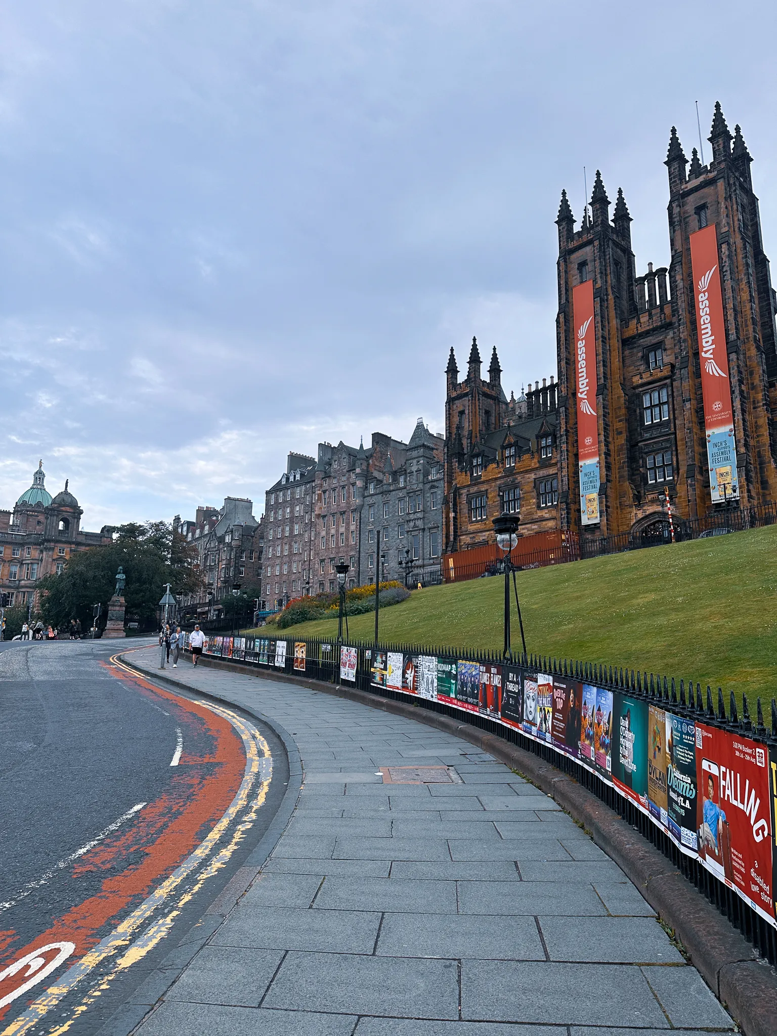 The Mound curving down past a fence of Fringe posters toward the Bank of Scotland's dome, the Assembly Hall's lawn climbing to the right