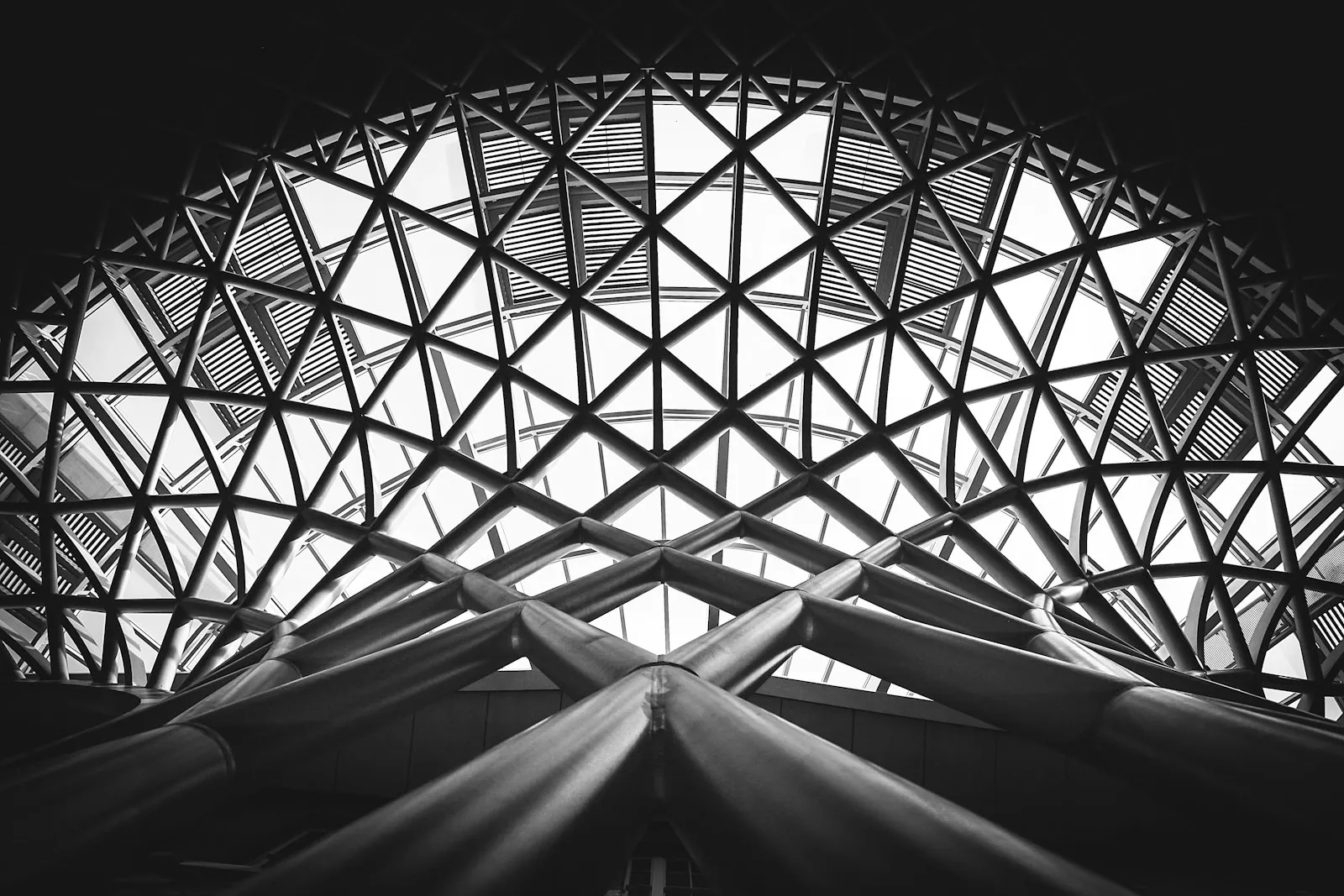 Looking up into a triangulated steel and glass roof, in black and white