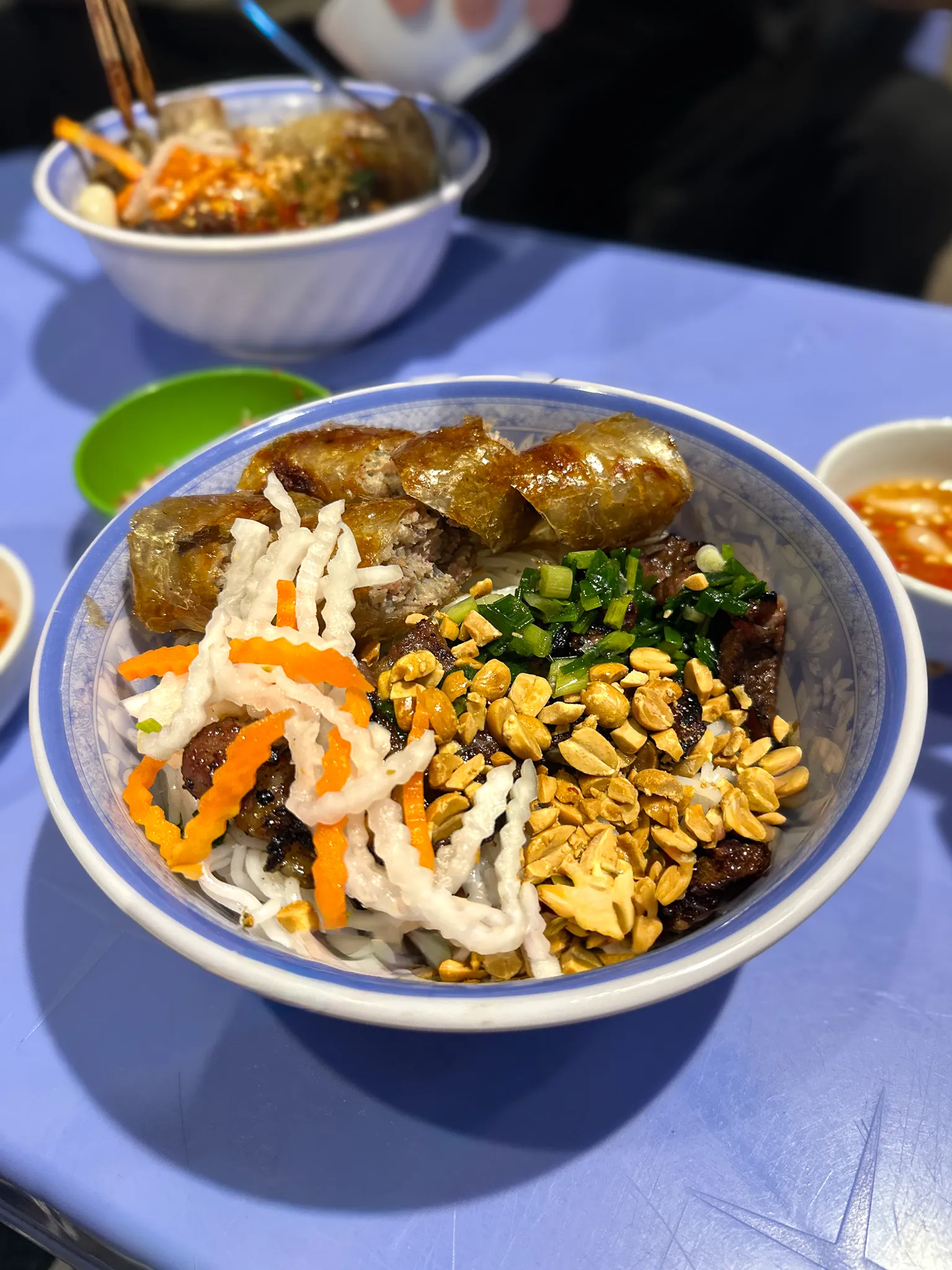 A bowl of bun thit nuong: crispy spring rolls, grilled pork, roast peanuts, pickled daikon and carrot over vermicelli
