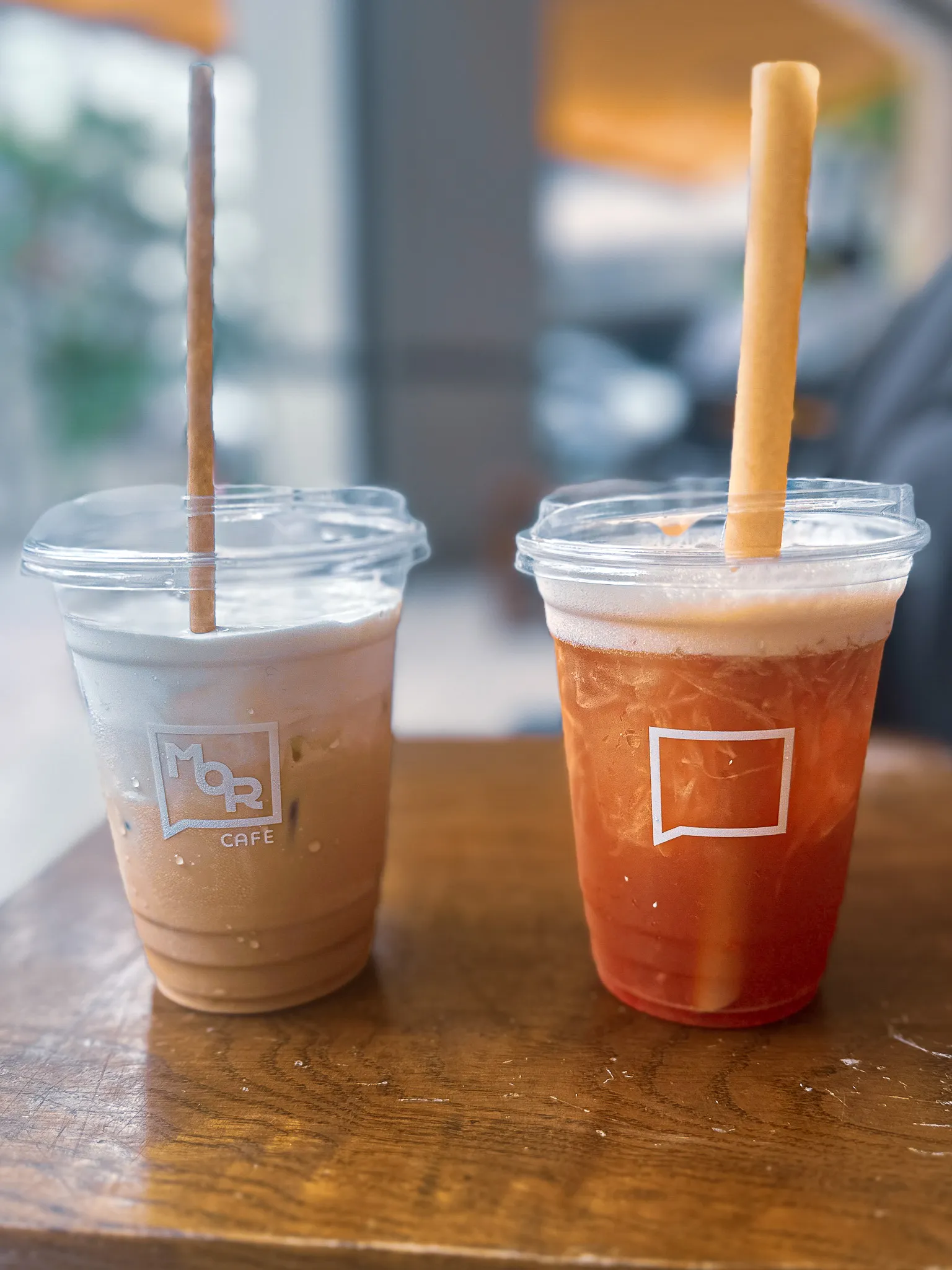 Two iced drinks with cookie straws on a worn wooden table, one milky coffee and one amber tea