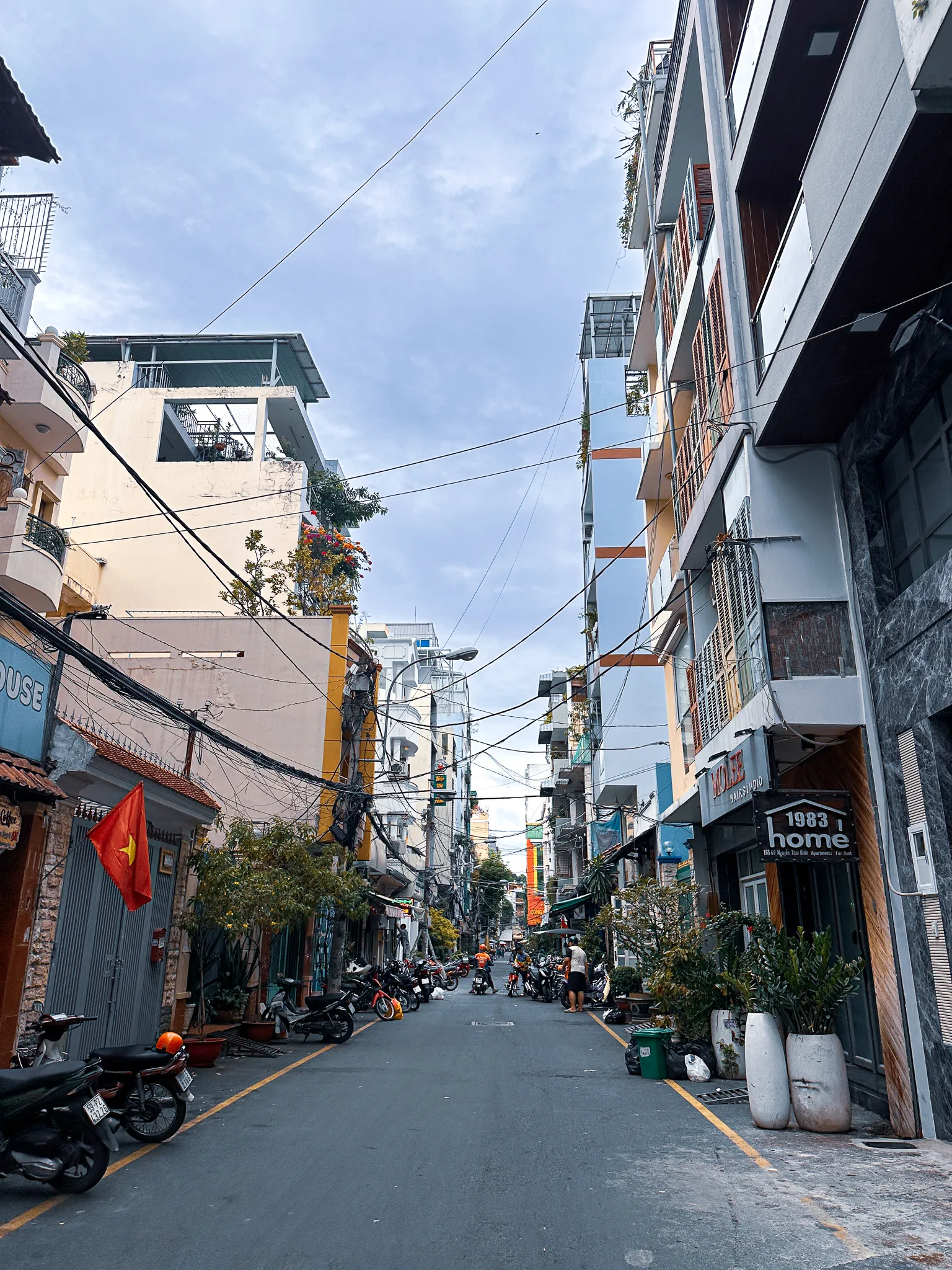 A quiet street of tube houses and parked motorbikes, a Vietnamese flag reaching out over the pavement