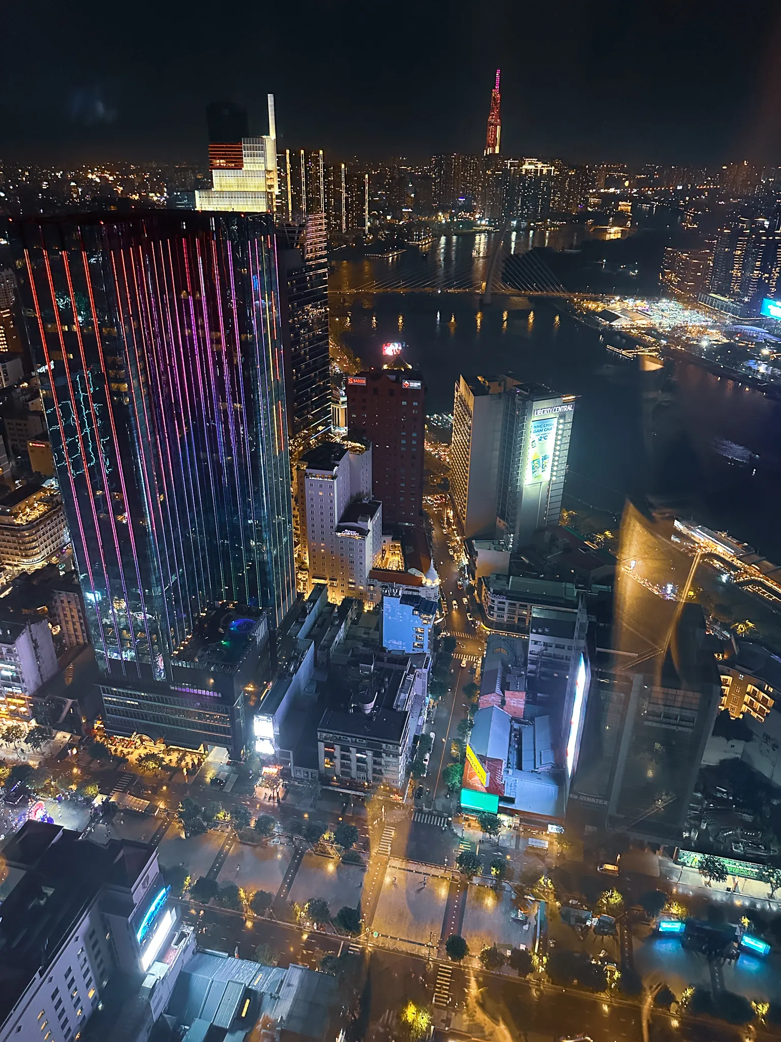 District 1 at night from high up, LED-striped towers and the lit cable-stayed bridge over the Saigon River, Landmark 81 far off