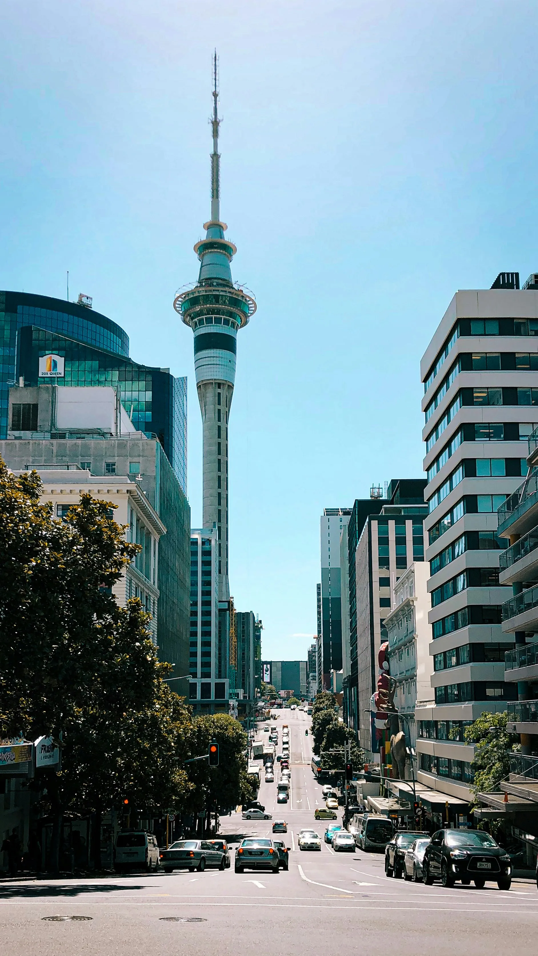 Queen Street rising between office towers with the Sky Tower's needle at the top of the view
