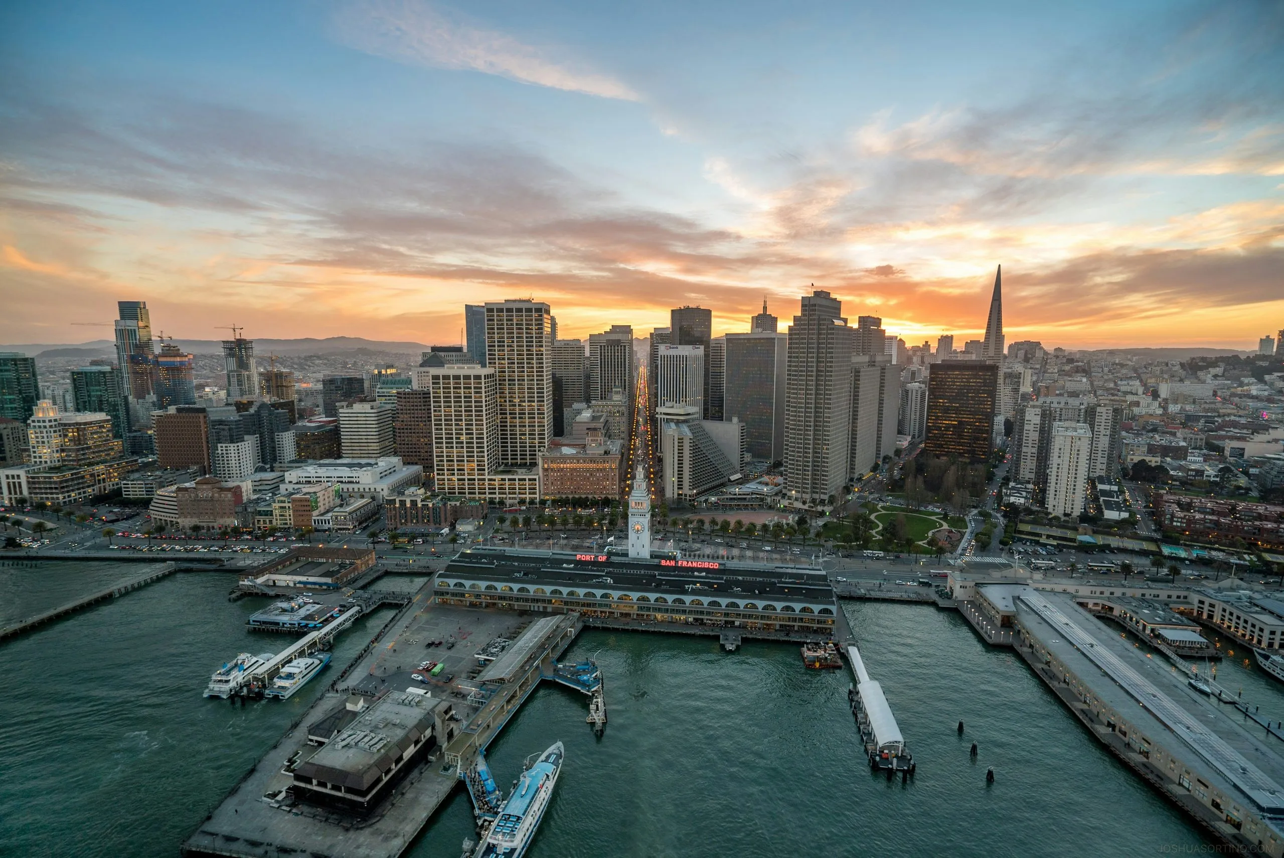 The downtown skyline and the Embarcadero's finger piers from above at sunset, boats moored along the water