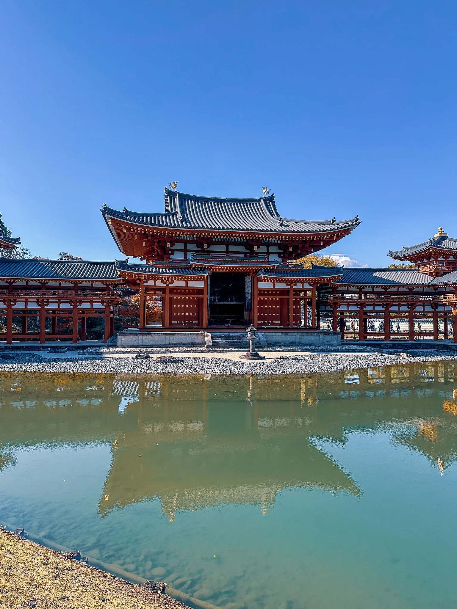 The Phoenix Hall at Byodo-in with its long red colonnades reaching out either side, mirrored in the still green water of its pond under a cloudless sky