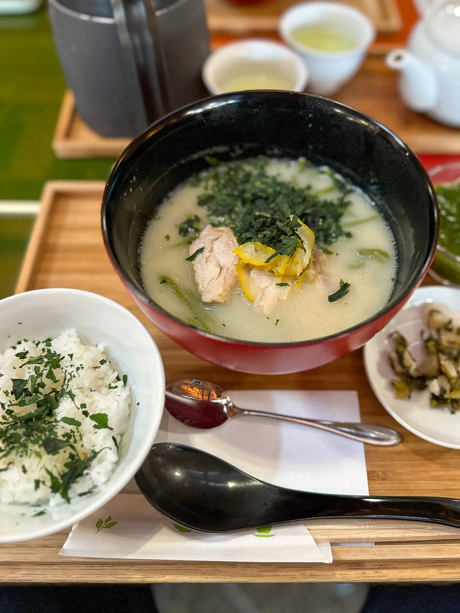 The same meal from above on a wooden tray - the bowl of milky broth with chicken and shredded yuzu, a bowl of rice flecked with herbs, small dishes of pickles and a white teapot