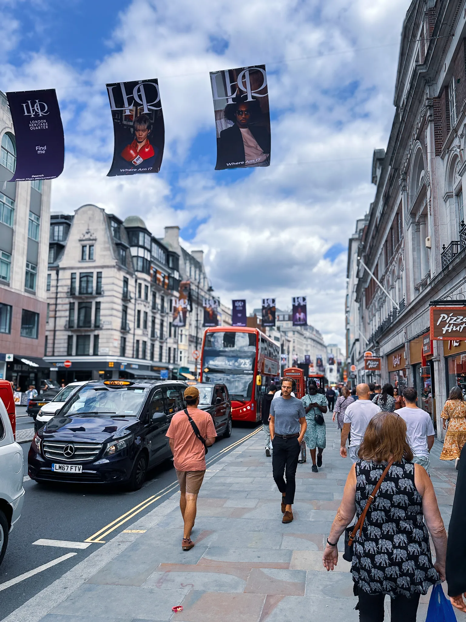 Banners strung above the Strand over stopped traffic, each printed with the words Where Am I?, a red bus and a black cab held at the lights and the pavements busy on both sides