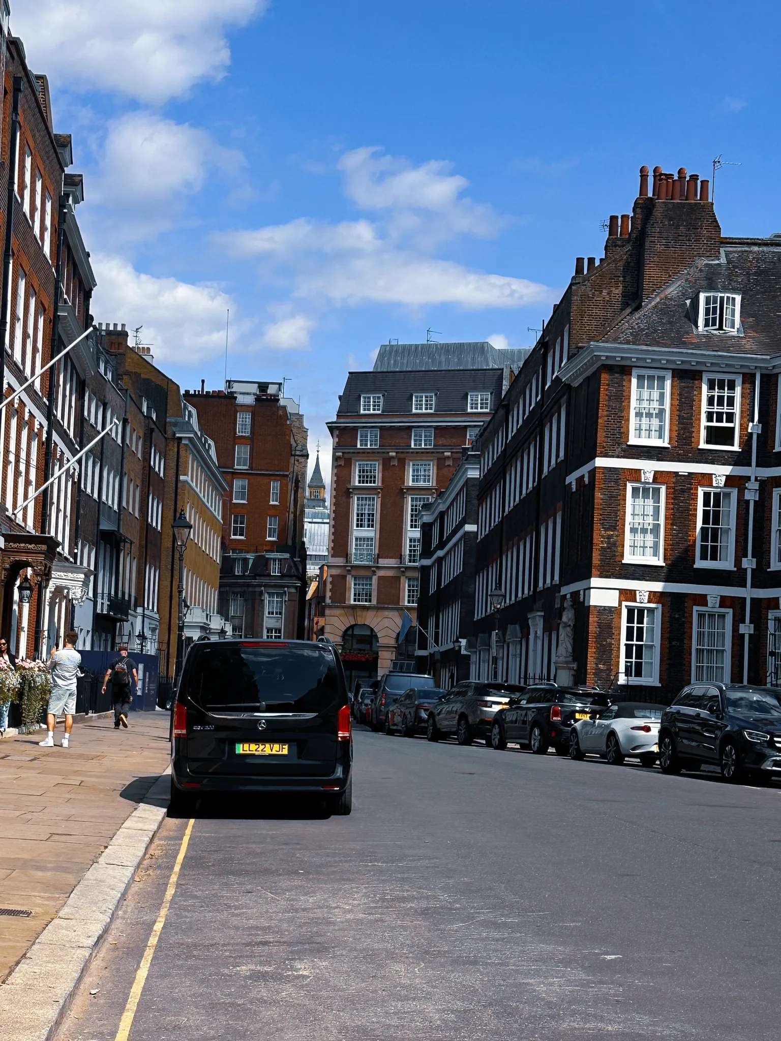 A quiet Westminster street of dark brick houses and white sash windows, cars parked down the right-hand side and the top of the Elizabeth Tower showing in the gap at the end