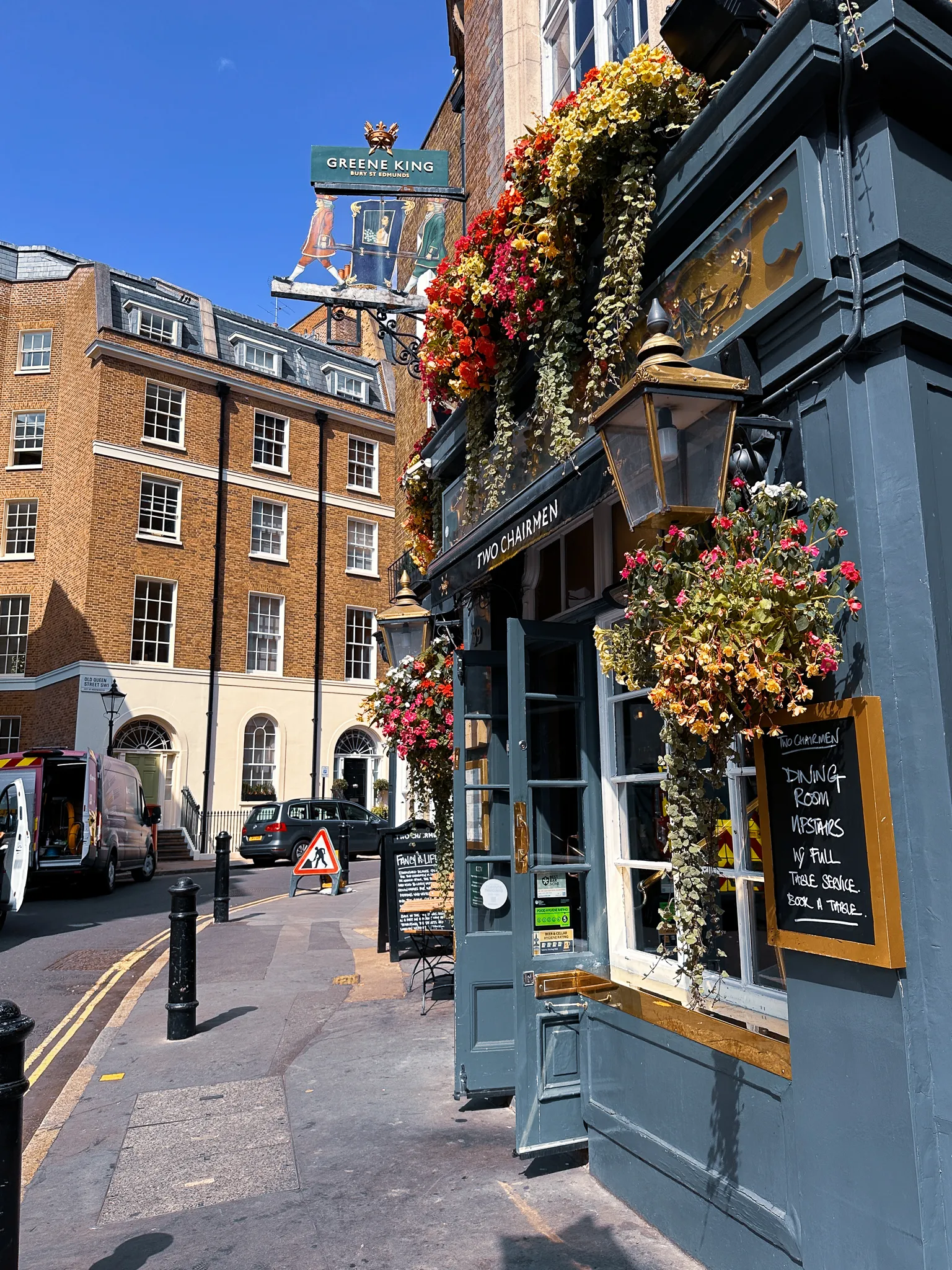 The corner of the Two Chairmen, a Greene King pub hung with baskets of flowers, a lantern over the door and a chalkboard offering the dining room upstairs