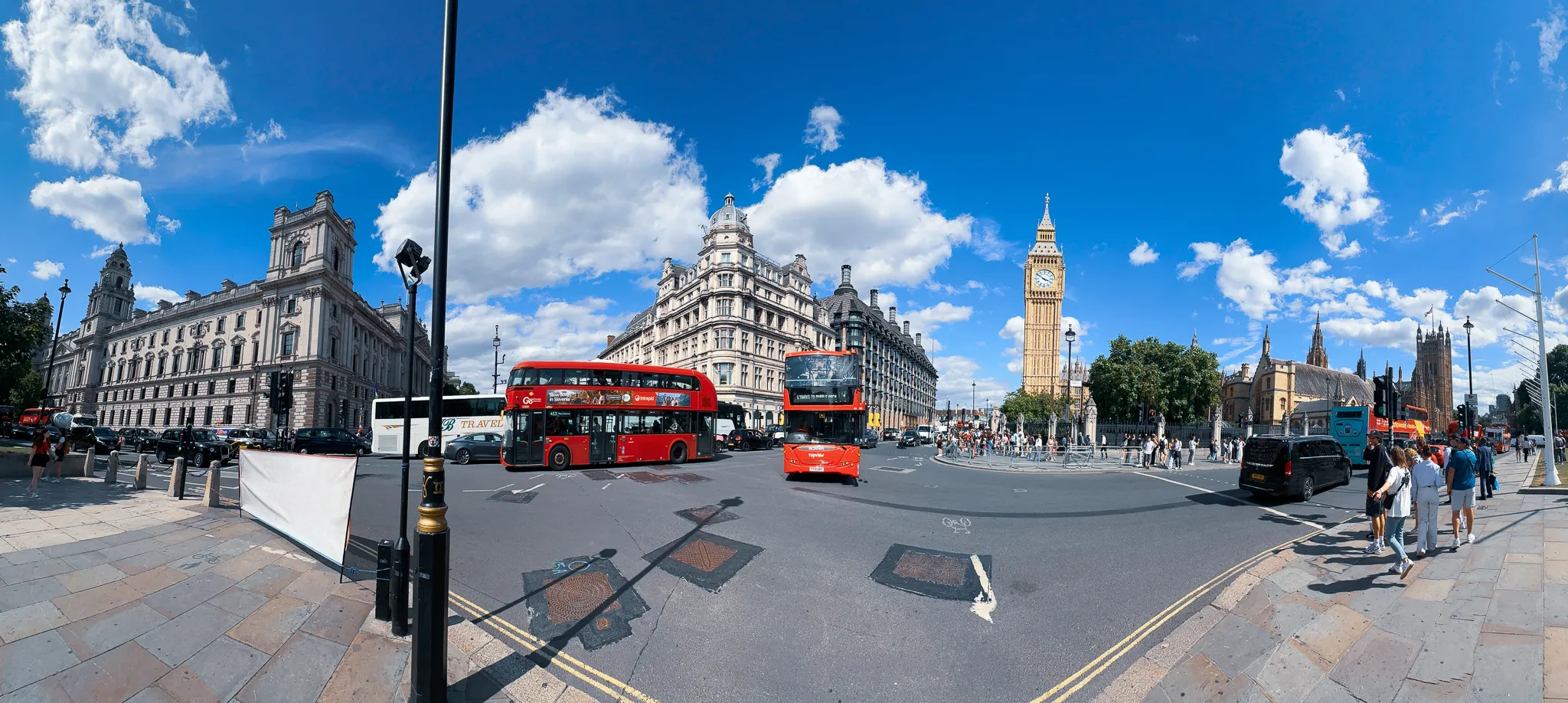 A wide sweep of Parliament Square - Whitehall's stone offices on the left, two red buses turning through the middle, the Elizabeth Tower and the Abbey's towers on the right and the pavement curving away in the foreground