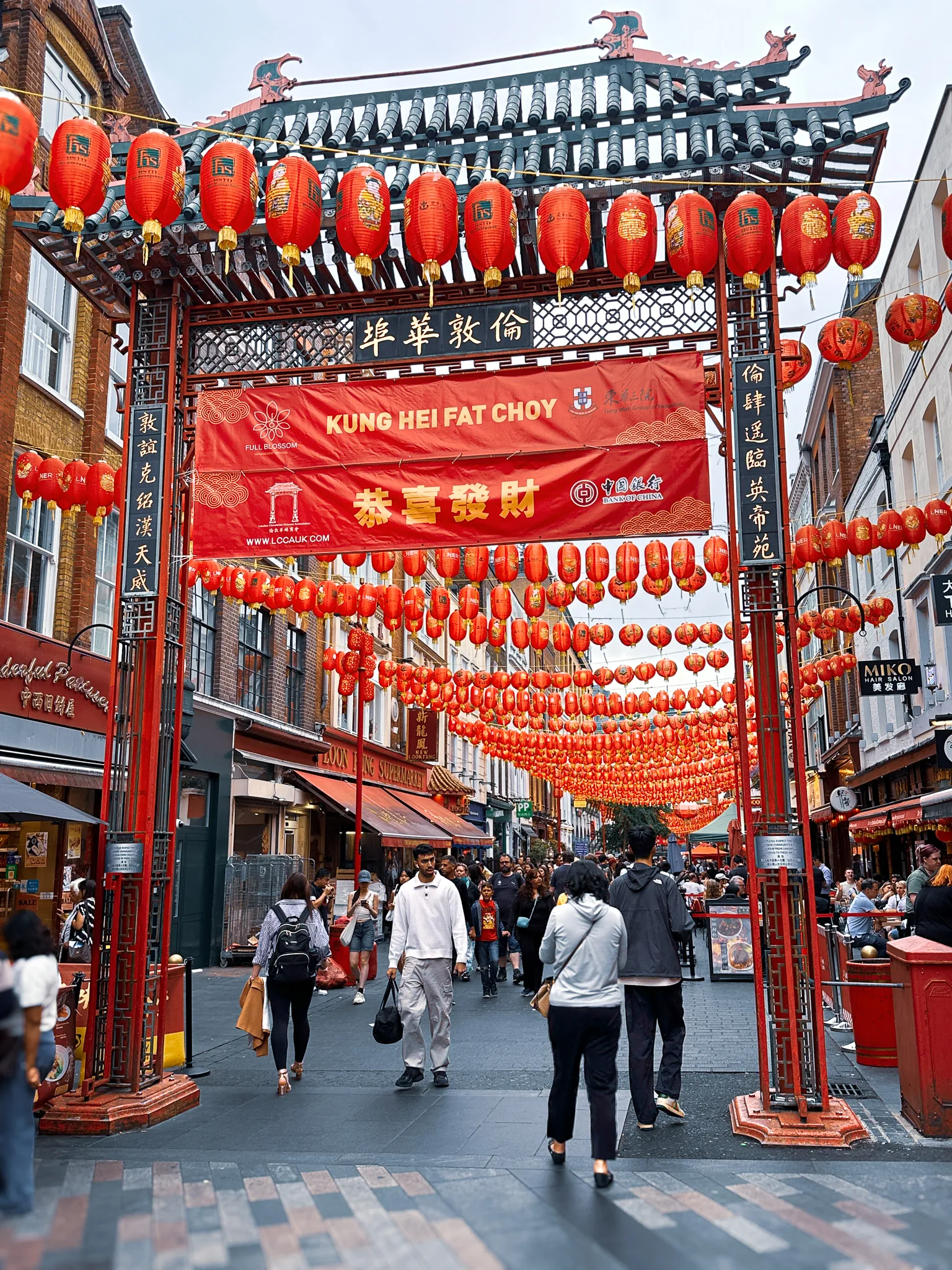 A Chinatown gate hung with rows of red lanterns, a banner reading Kung Hei Fat Choy stretched beneath its roof and the street behind it filled with lanterns and people
