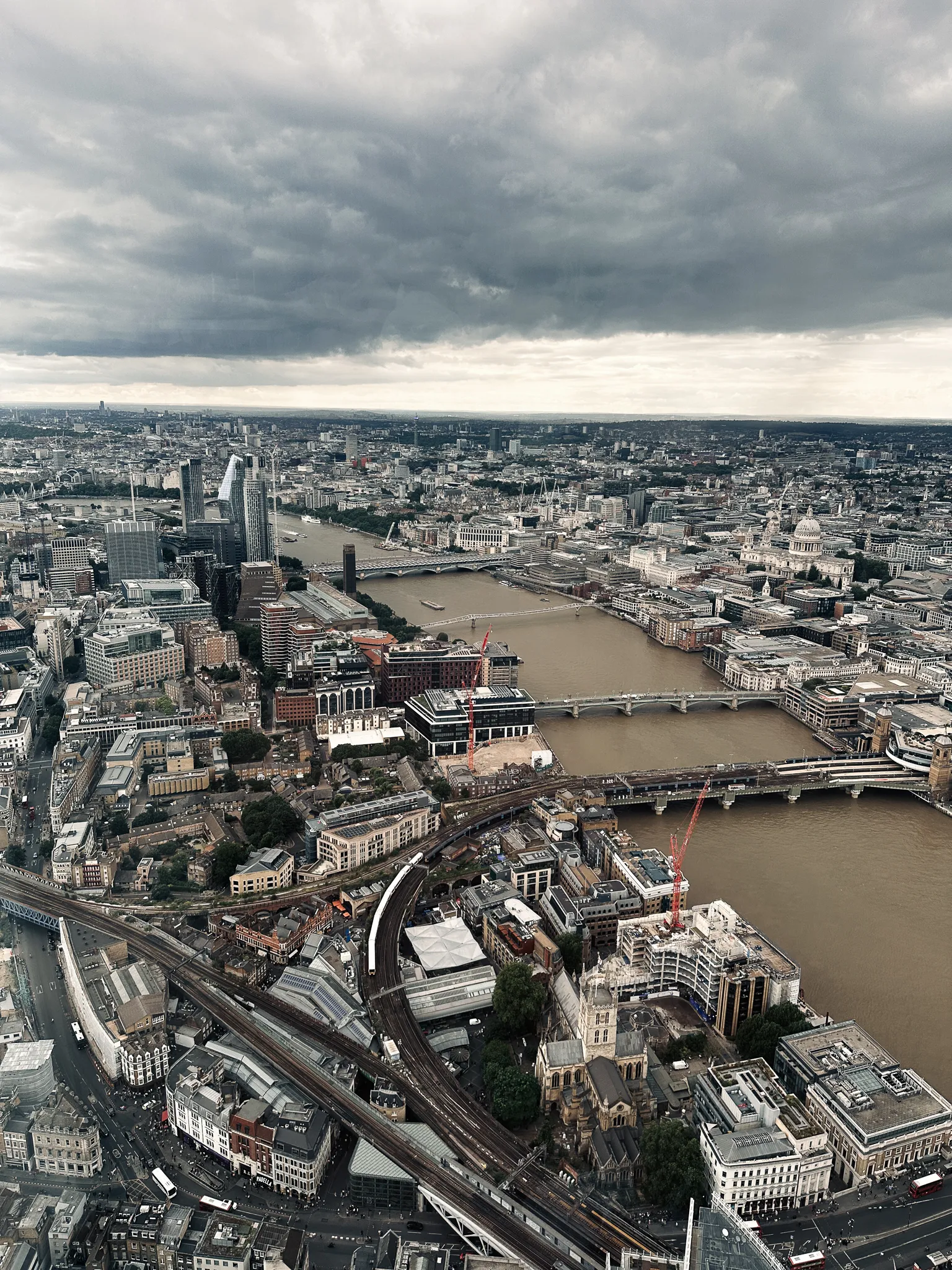 West from the same window - the Thames running away under three bridges, the dome of St Paul's on the right, railway lines curving in below and a bank of dark cloud over all of it