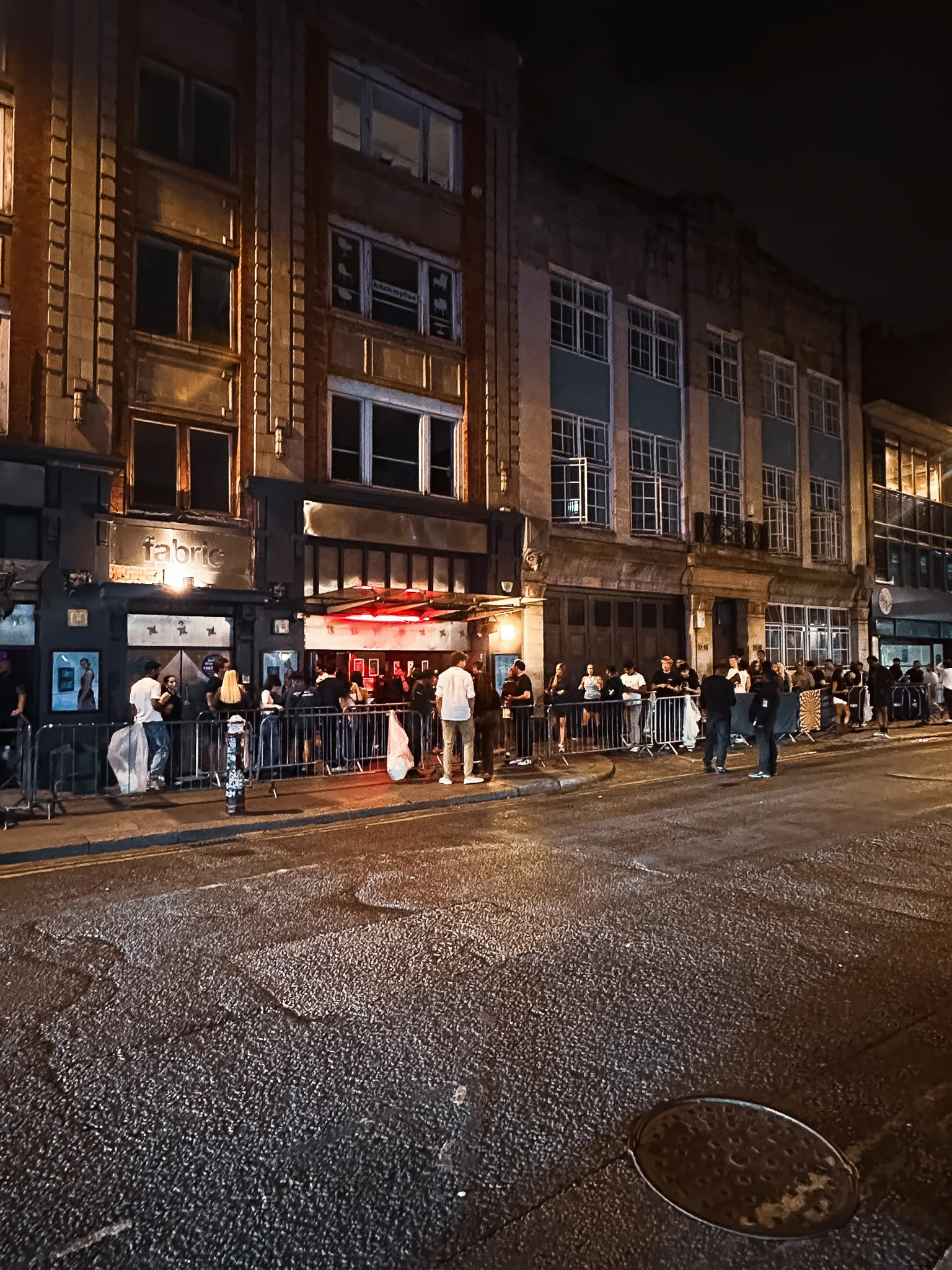 The street outside the club at half past two, the queue still running along the barriers, the red glow of the entrance and the road wet in front of it