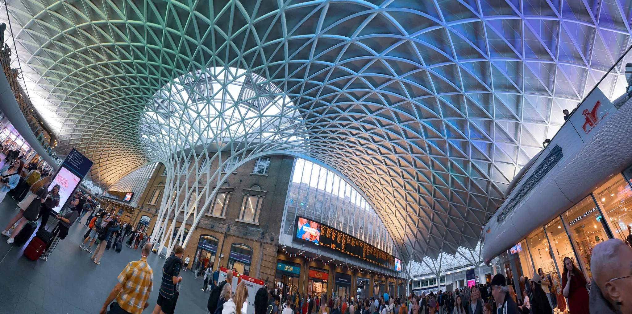 The white lattice roof of King's Cross fanning out over the concourse, departure boards and shopfronts underneath it and travellers crossing with their luggage
