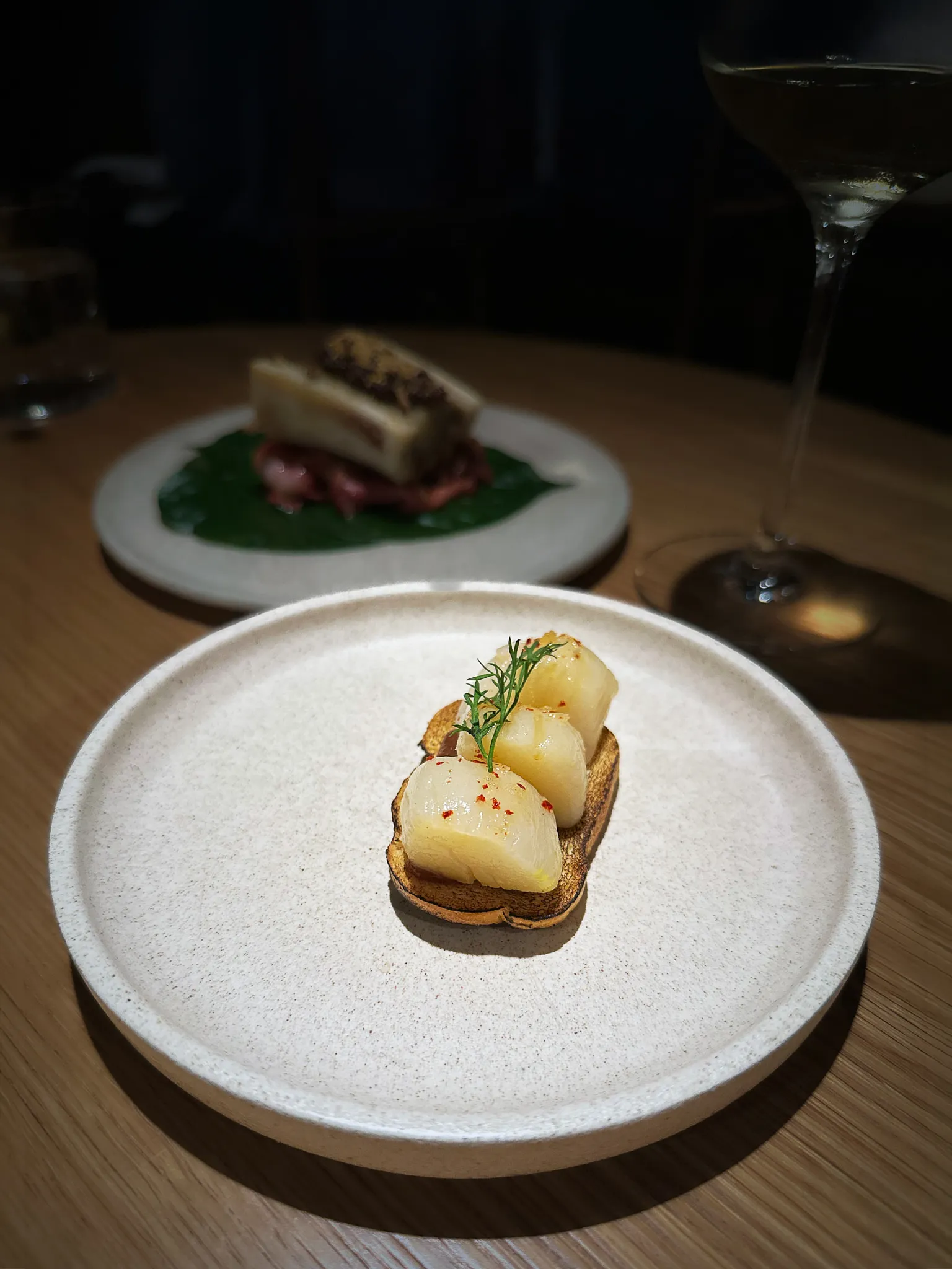 Three scallops on grilled bread with a frond of dill, on a pale plate in a dark dining room