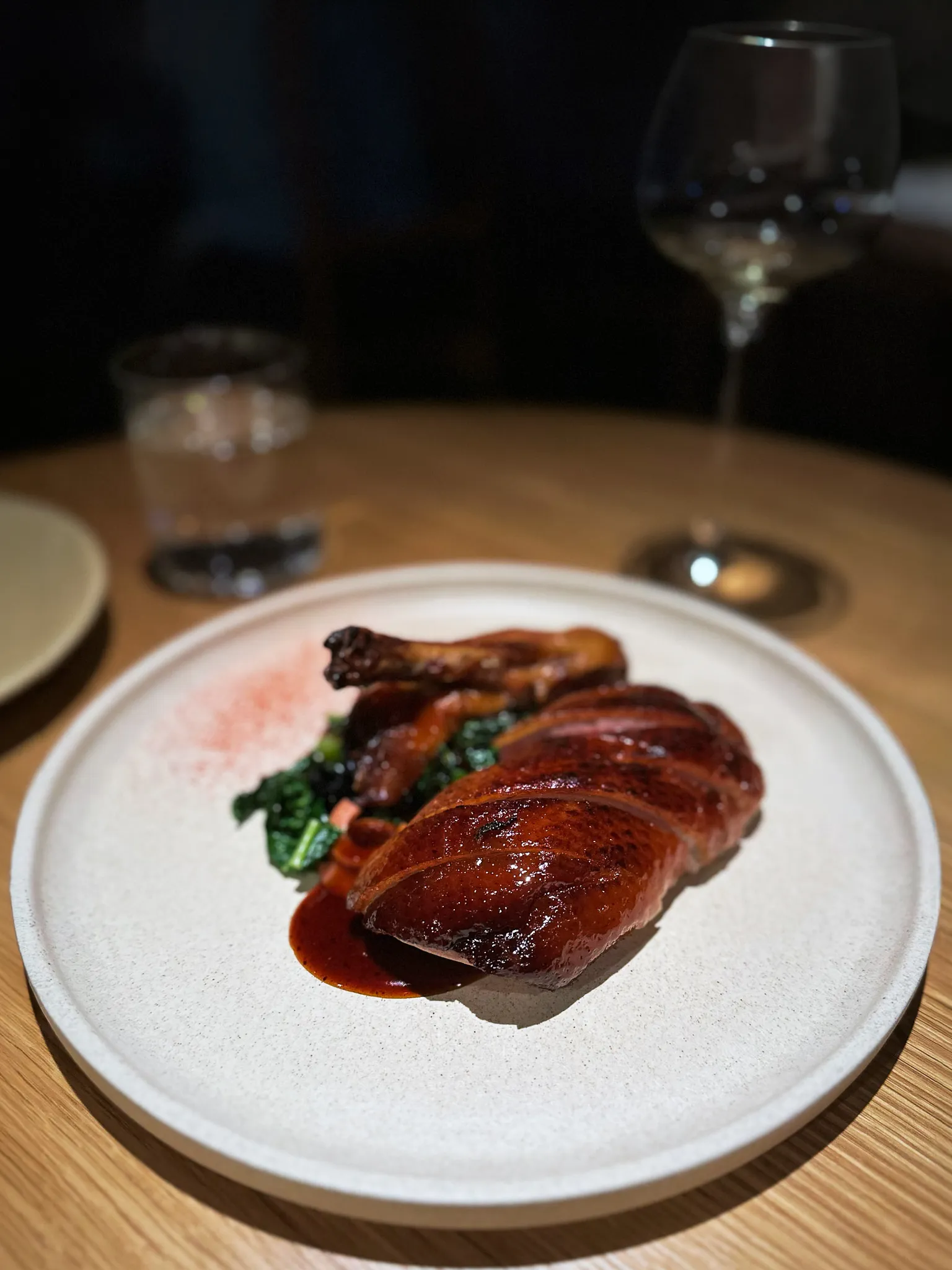 Sliced lacquered duck breast and a leg over greens in a dark sauce
