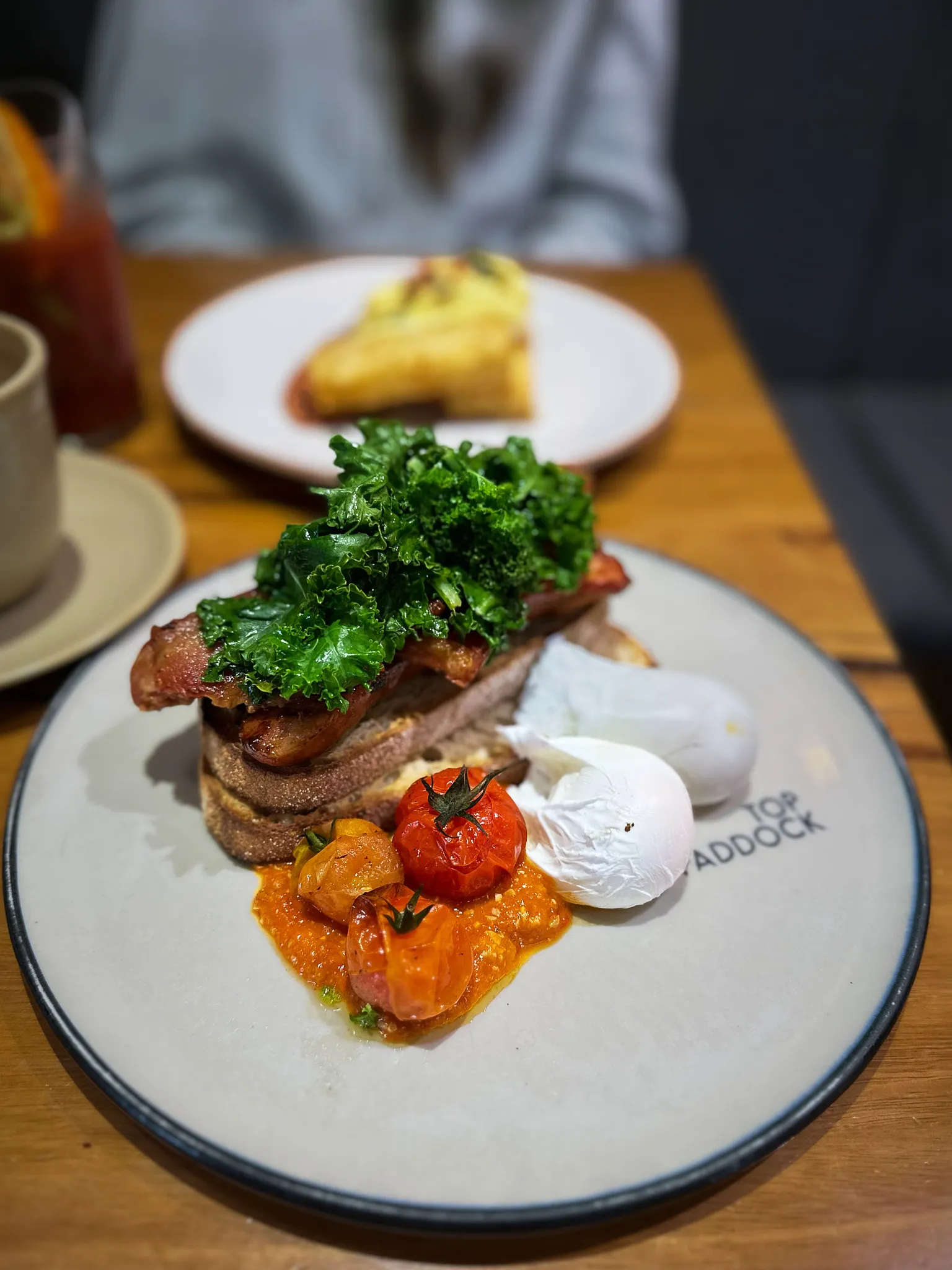 Bacon, crisped kale, poached eggs and blistered tomatoes on sourdough, on a plate branded Top Paddock