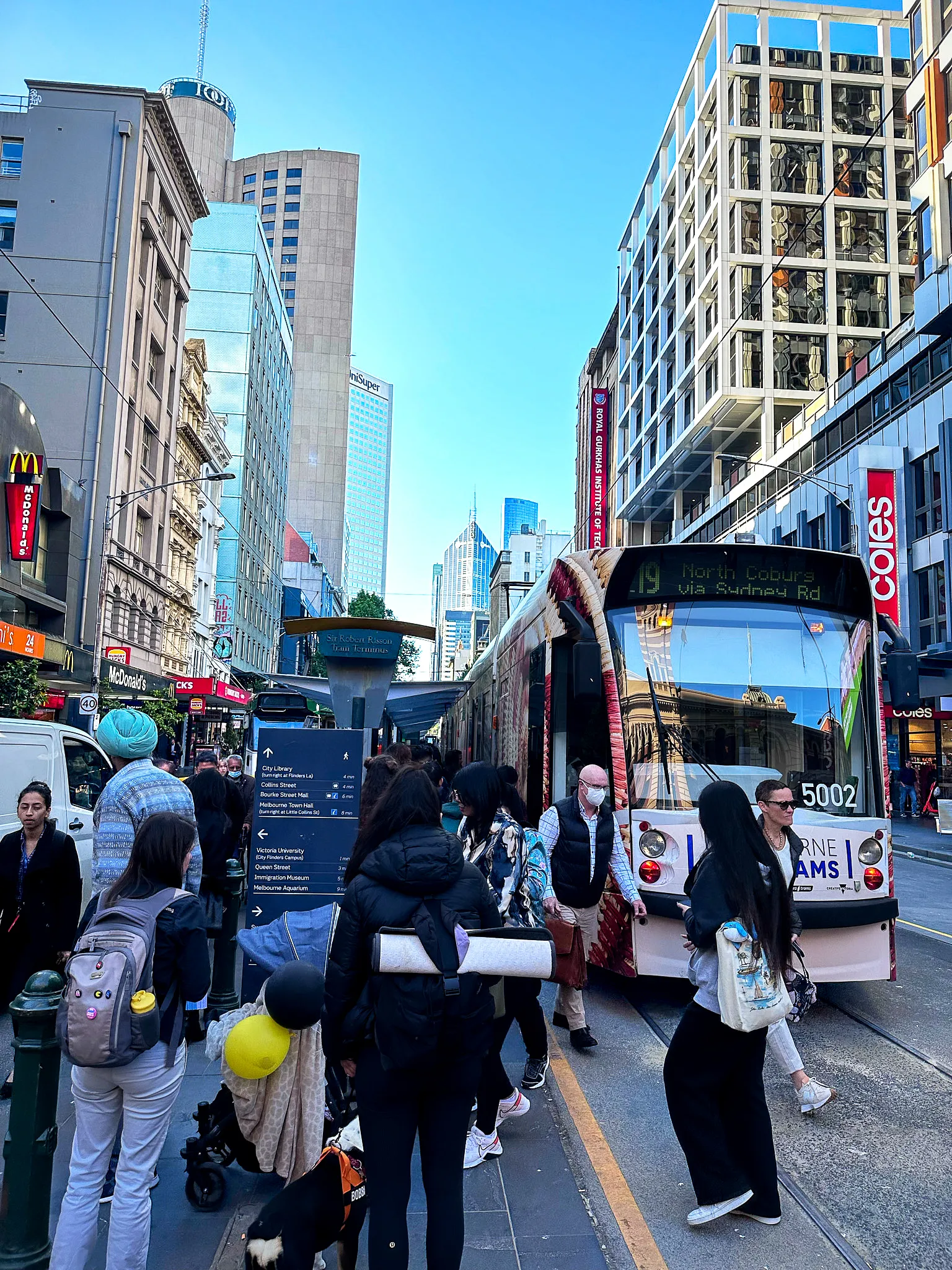 A crowd boarding tram 5002 to North Coburg on Bourke Street Mall, city towers behind
