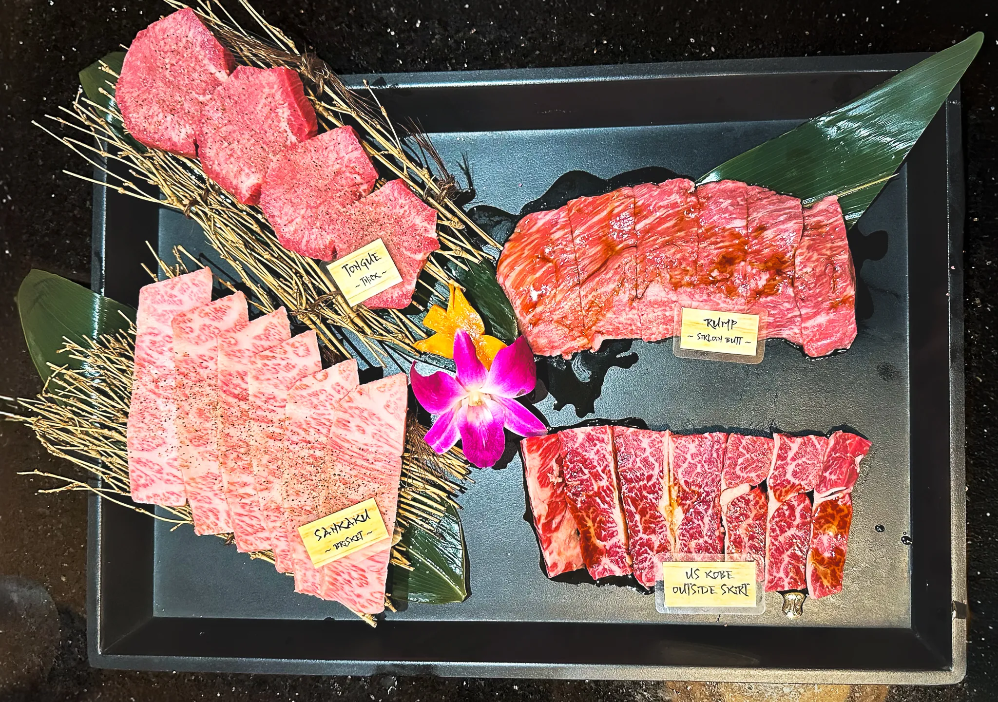 Trays of labelled wagyu - tomahawk, rump, sankaku, US Kobe outside skirt - on straw and banana leaf
