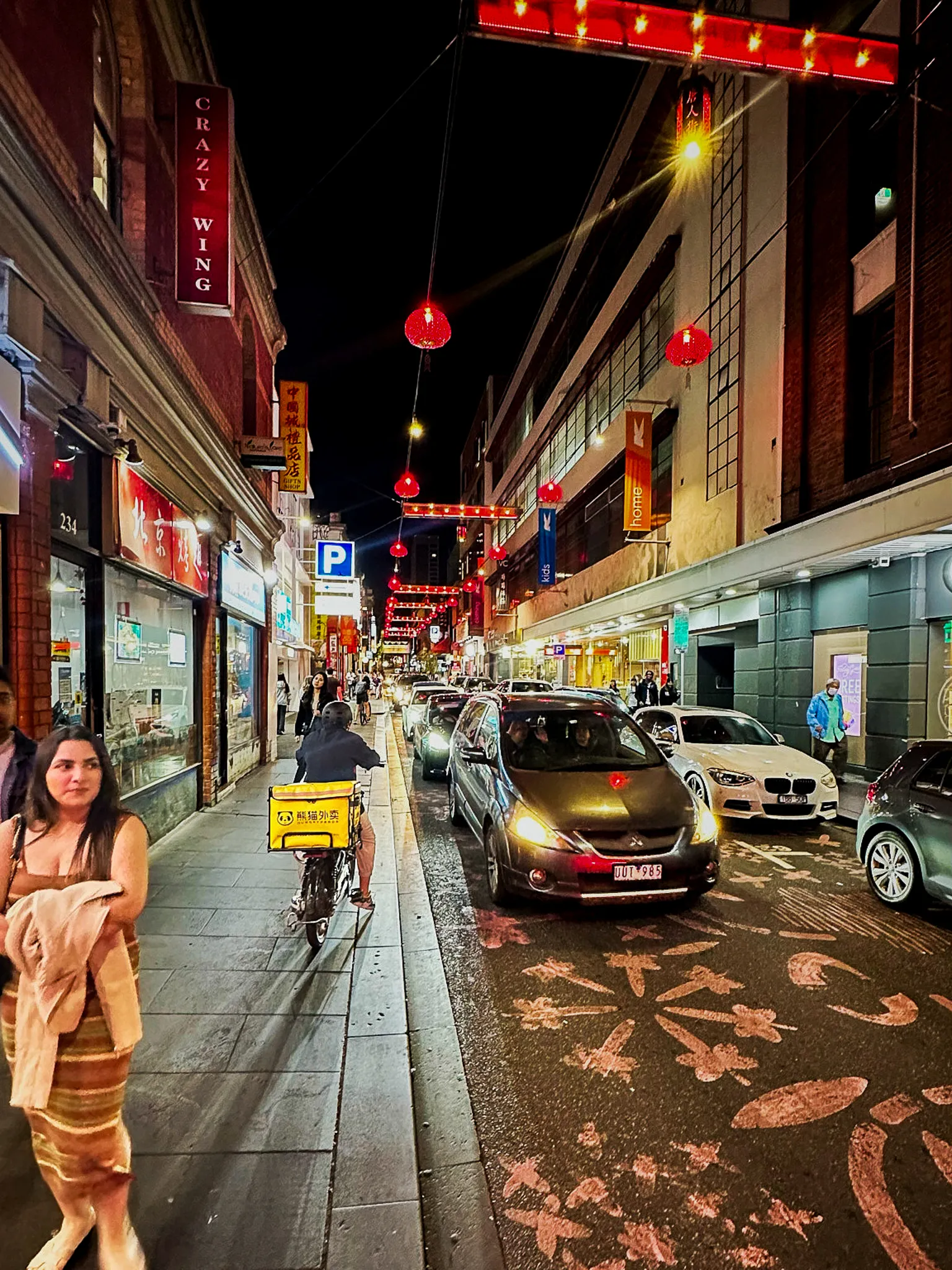 Chinatown at night, red lanterns strung above the street and cars queued between shopfronts