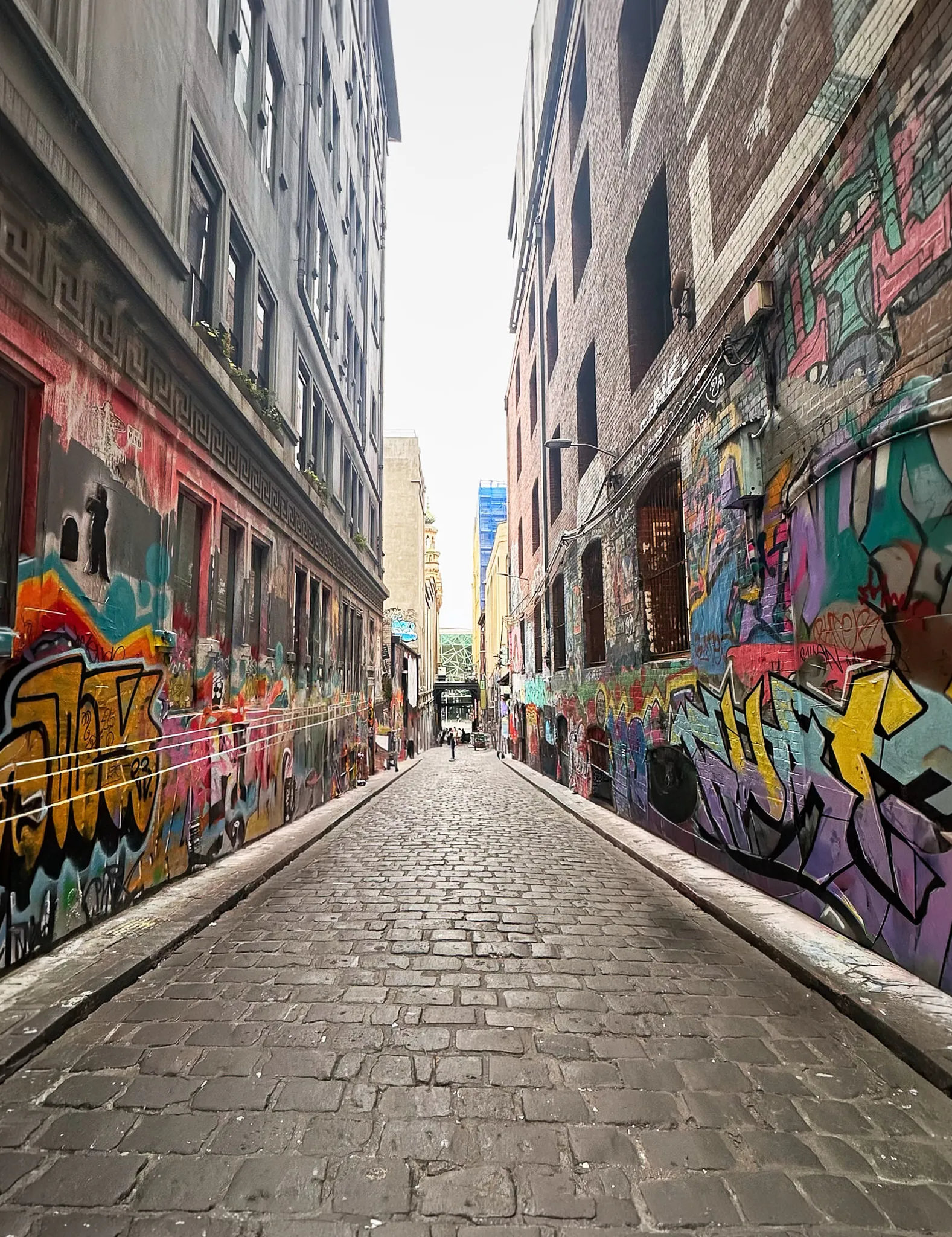 A bluestone laneway walled in graffiti, one person photographing at the far end
