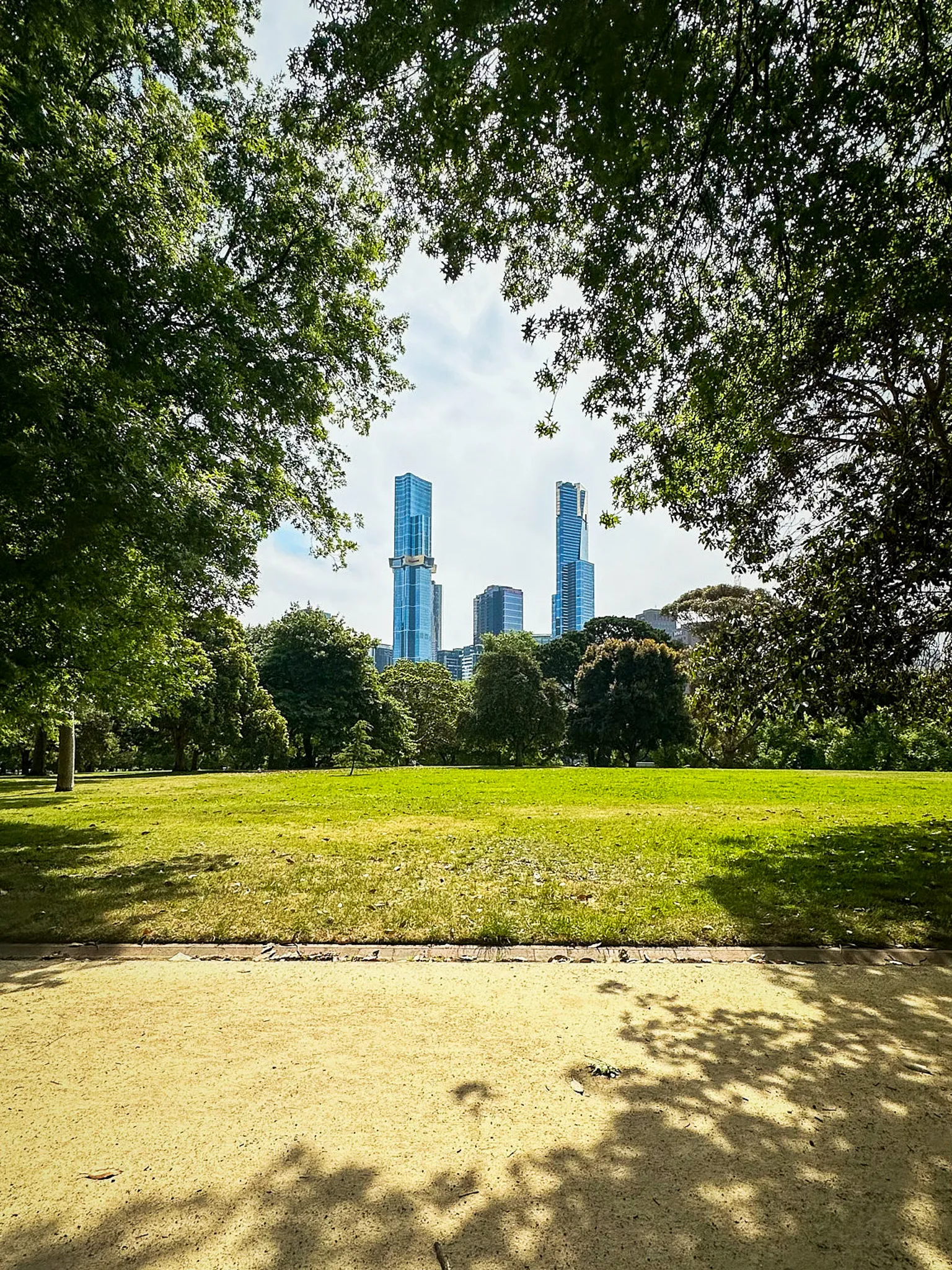 A park lawn framed by dark trees, two pale blue towers standing beyond