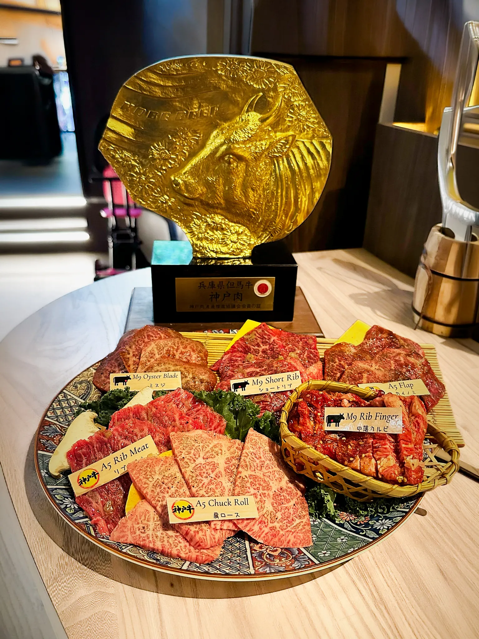 A platter of labelled A5 wagyu cuts in front of a gold Kobe bull trophy