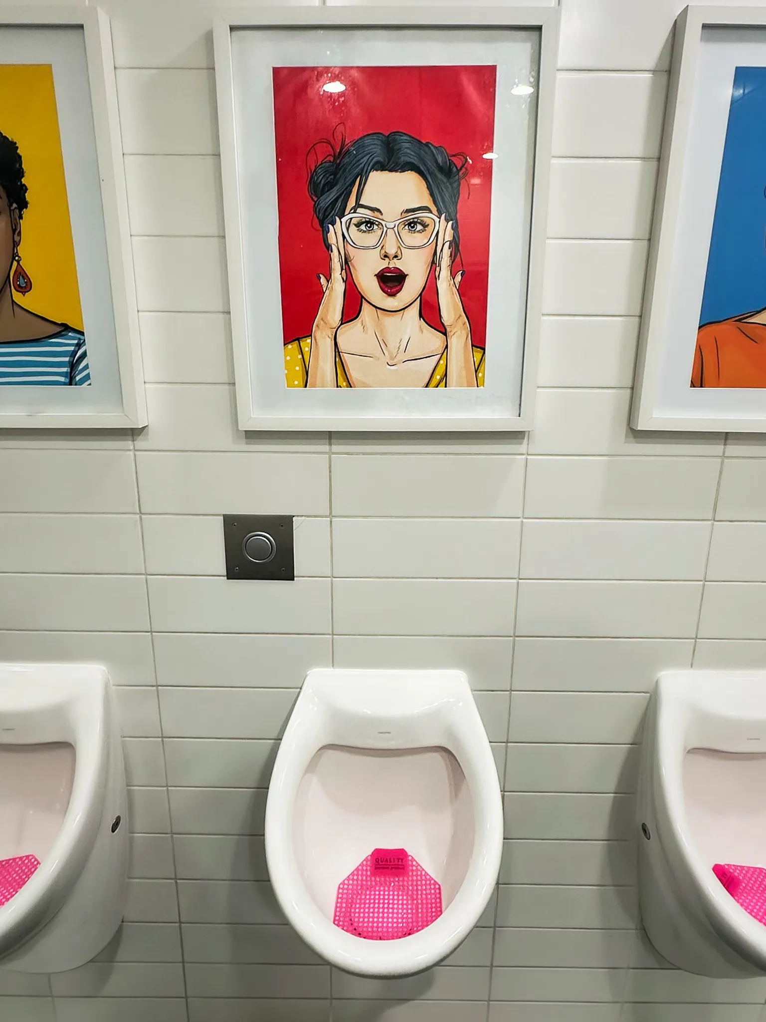 Three urinals below framed pop-art portraits on white tile