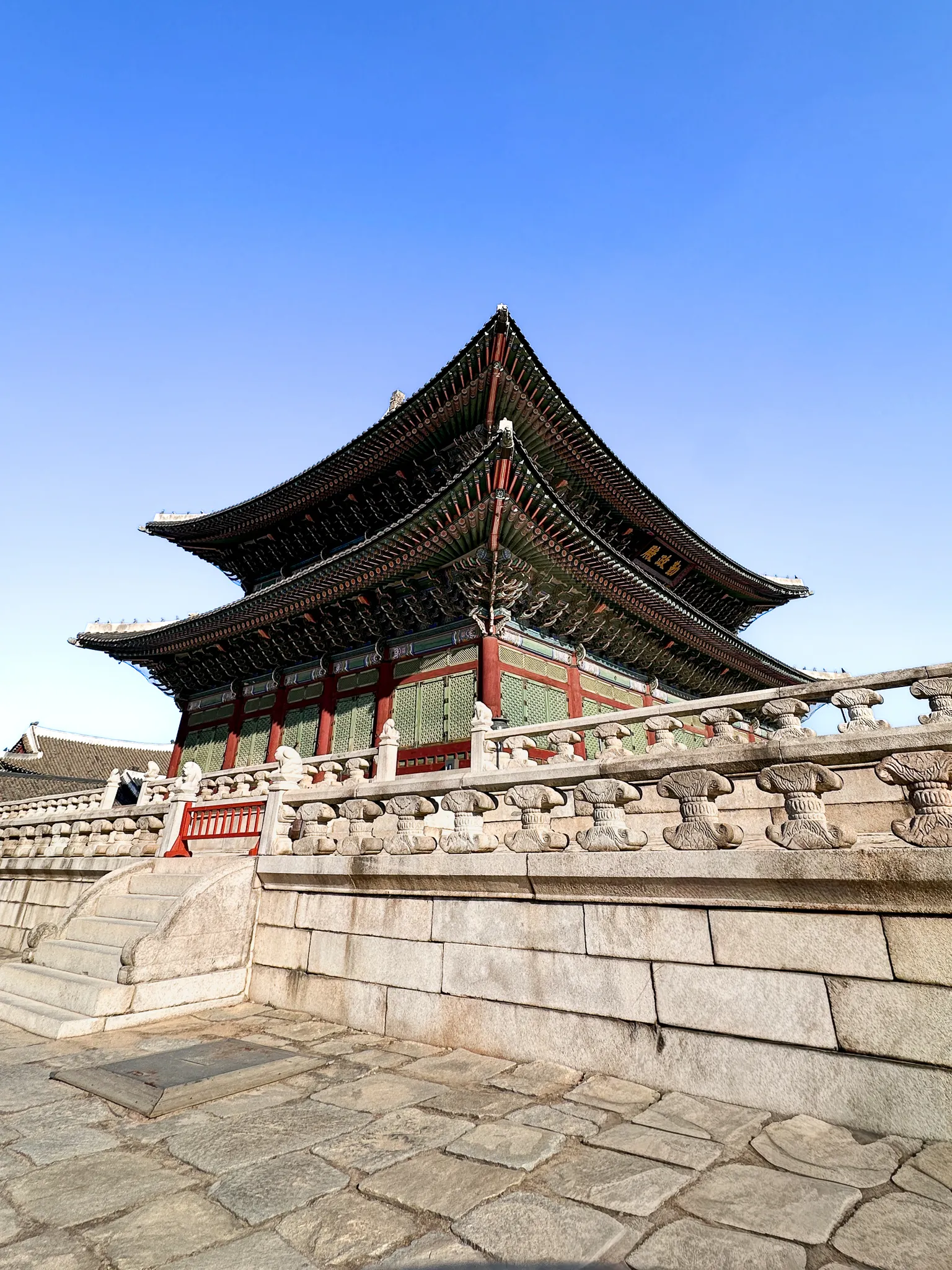 The double-roofed throne hall seen from below its stone terrace, the carved balustrade and its small stone animals running across the front, sky empty behind
