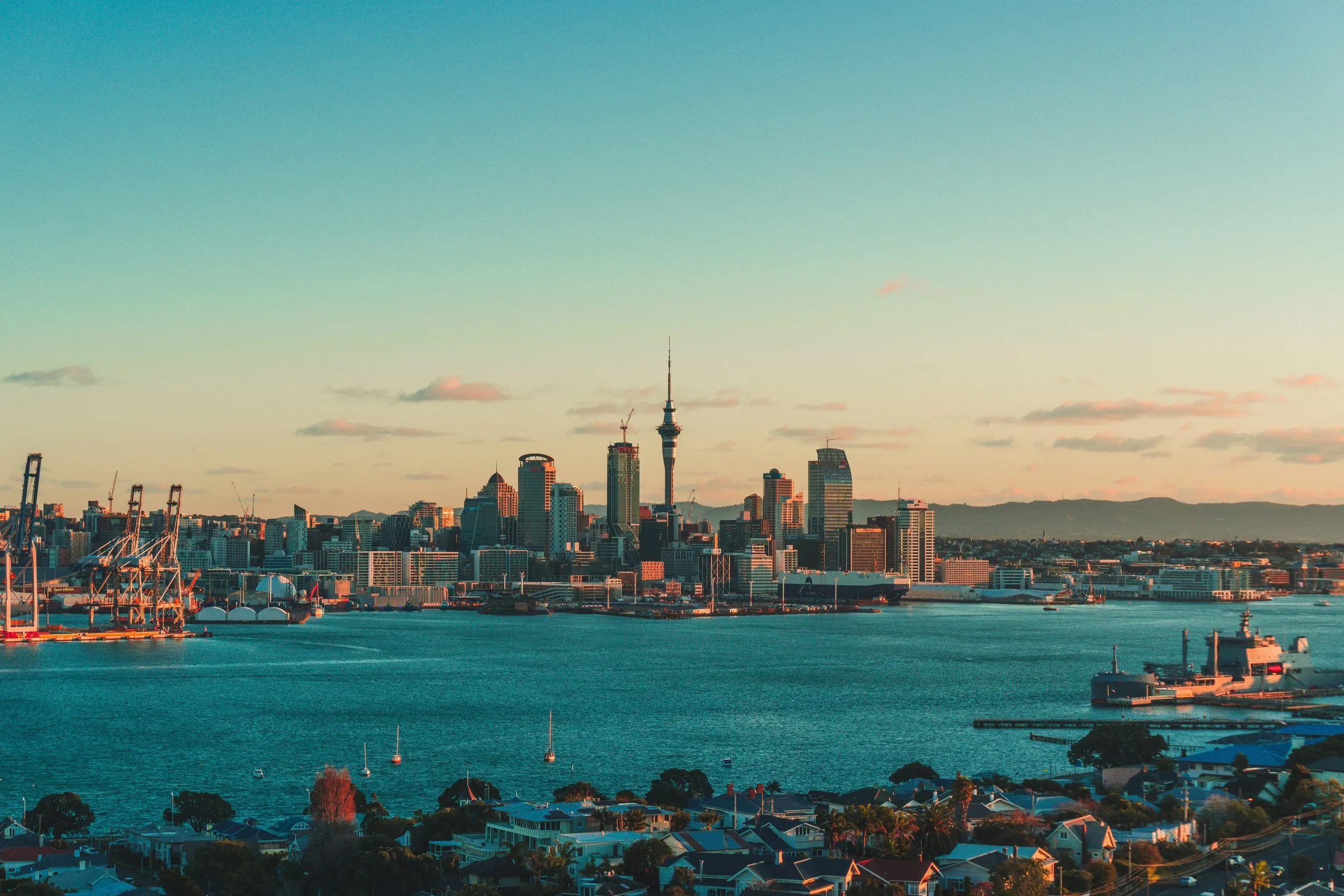 The city and harbour from a hill at dusk, the Sky Tower among the towers and port cranes along the waterfront