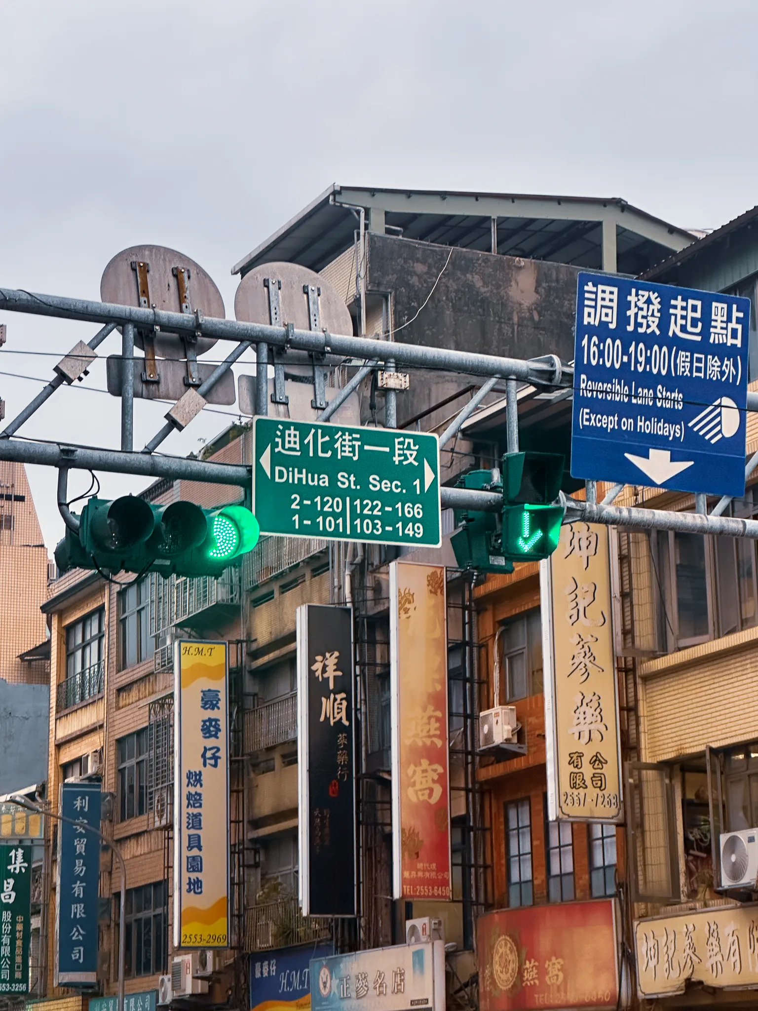 A green sign for Dihua St. Sec. 1 under a tangle of traffic lights and a blue reversible-lane notice, vertical shop banners for bird's nest and ginseng stacked down the buildings below