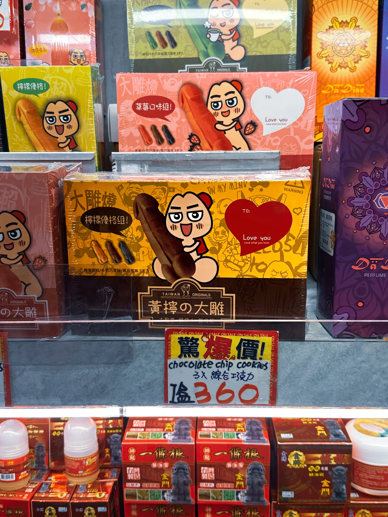 A souvenir shelf of novelty biscuit boxes with cartoon faces printed on them, a hand-lettered sale sign underneath reading chocolate chip cookies, 360