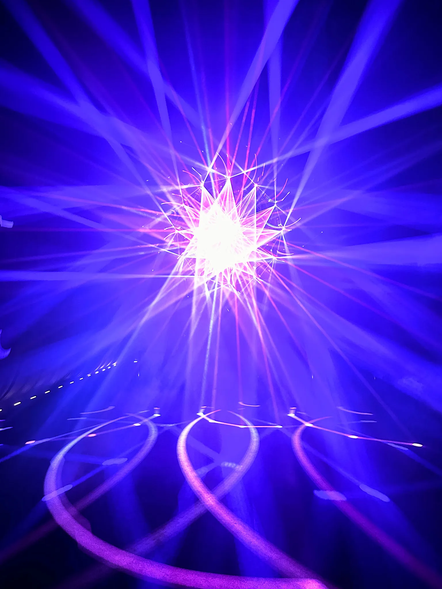 Blue and pink laser beams fanning out from a single bright point in a dark room