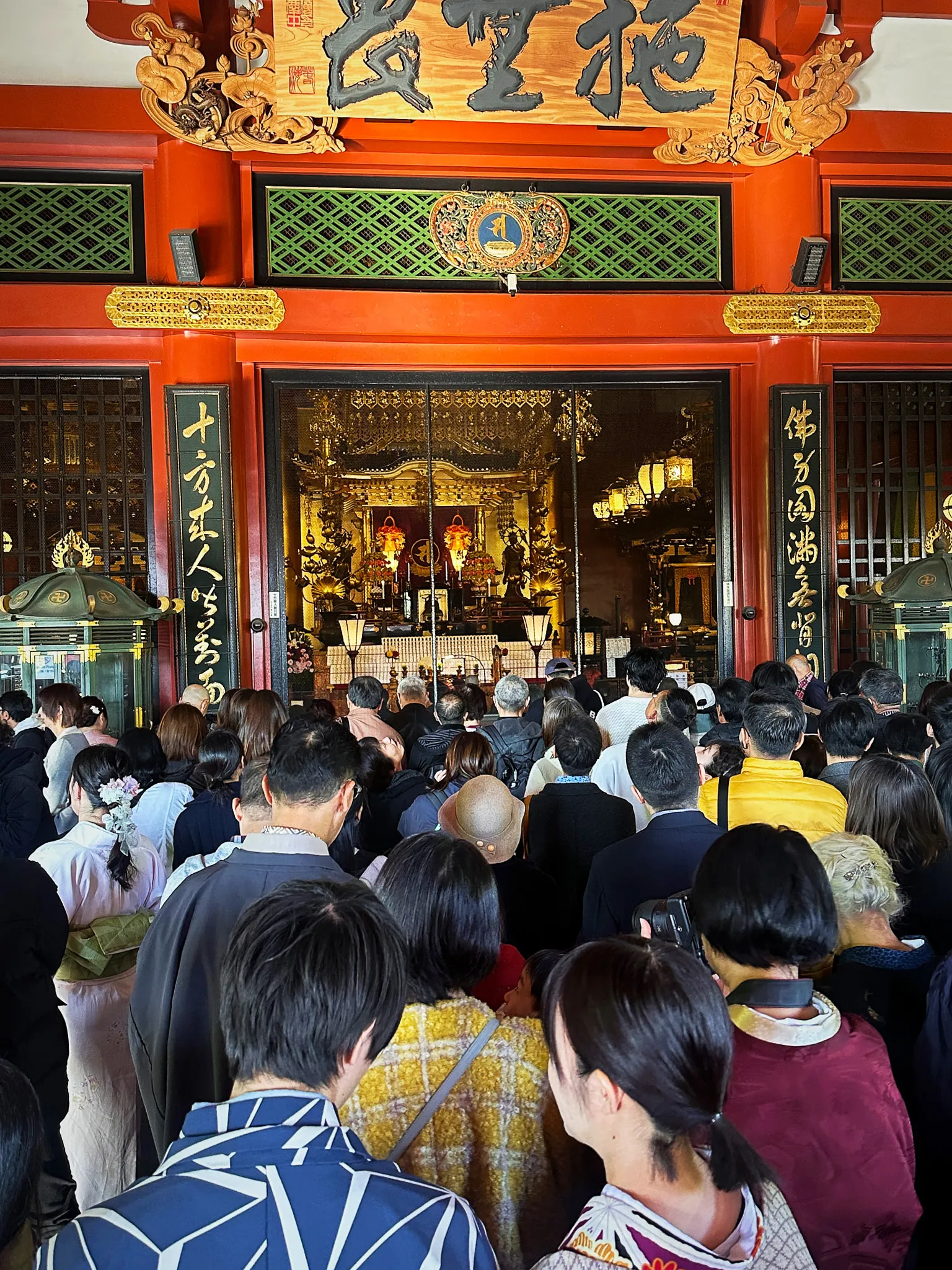 The gold altar inside Senso-ji's main hall seen over a packed crowd, carved and lacquered beams above