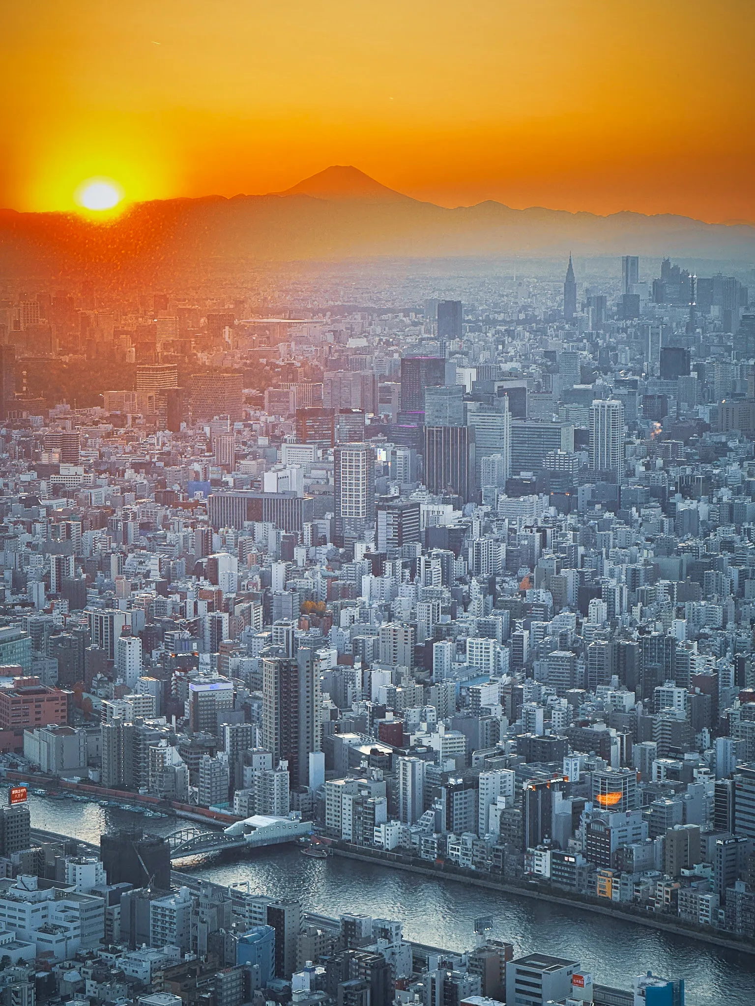 Sunset over Tokyo from high above, Mount Fuji in silhouette on the horizon and the city spreading out below in haze