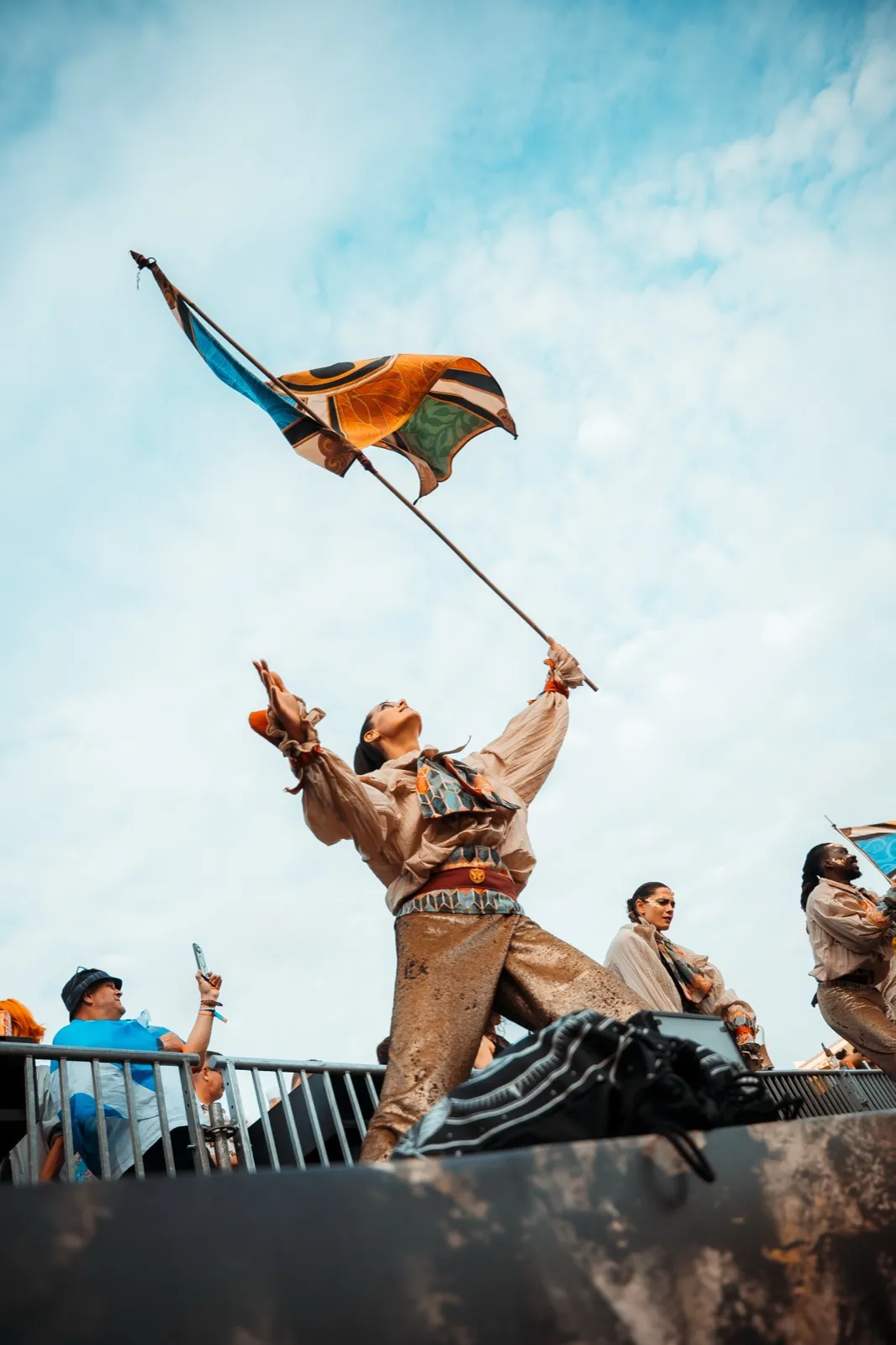 A man standing on a barrier holding a large flag out against a bright, near-white sky