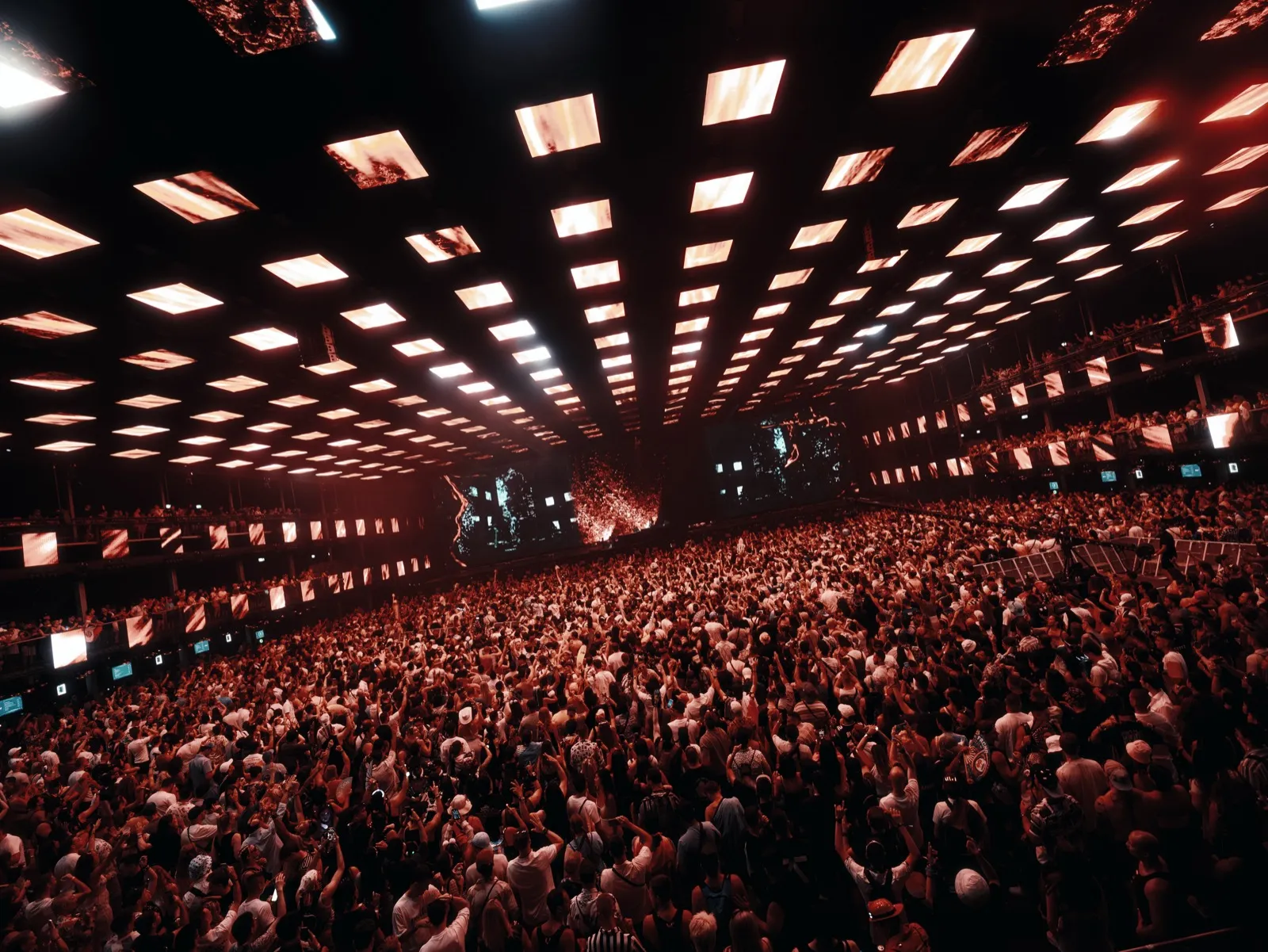 A packed indoor stage seen from the back, a grid of red ceiling lights running the whole length of the roof