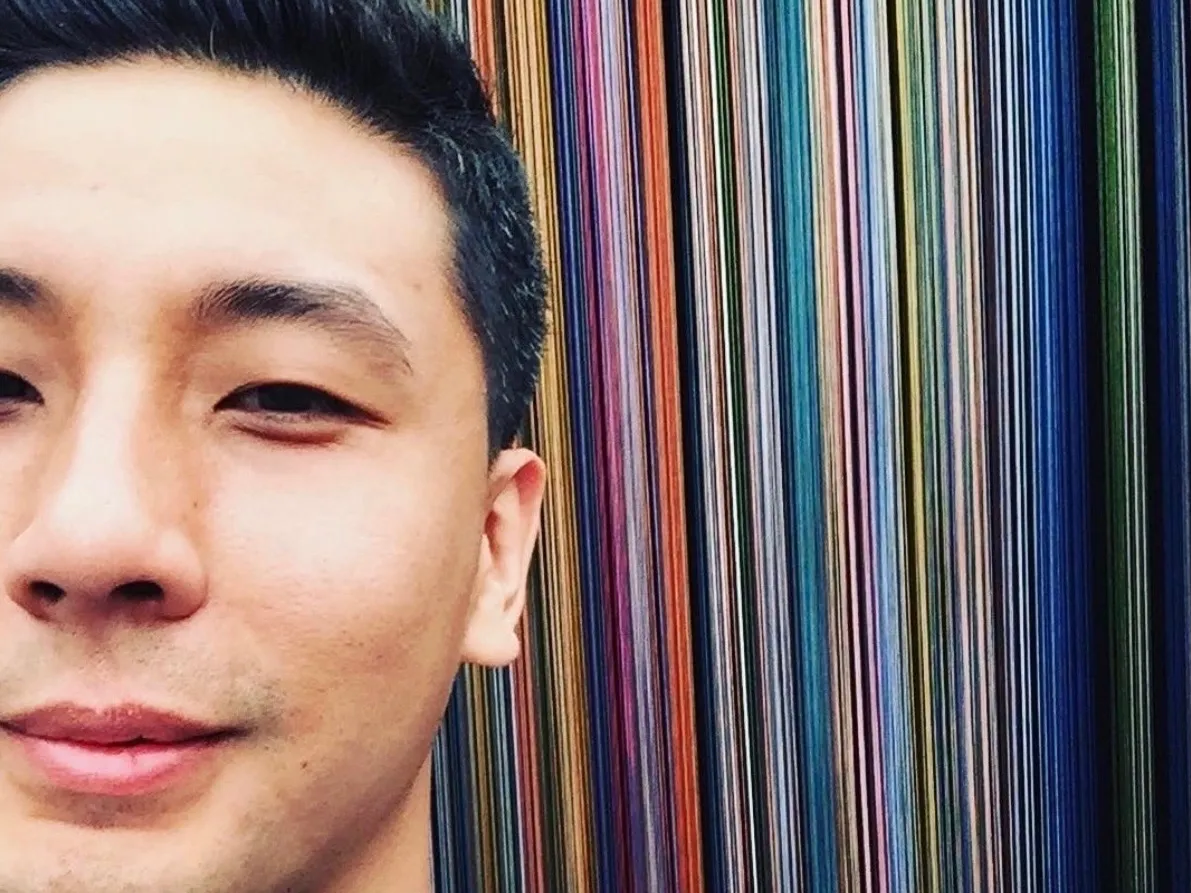 Trung, smiling in front of a wall of colored stripes