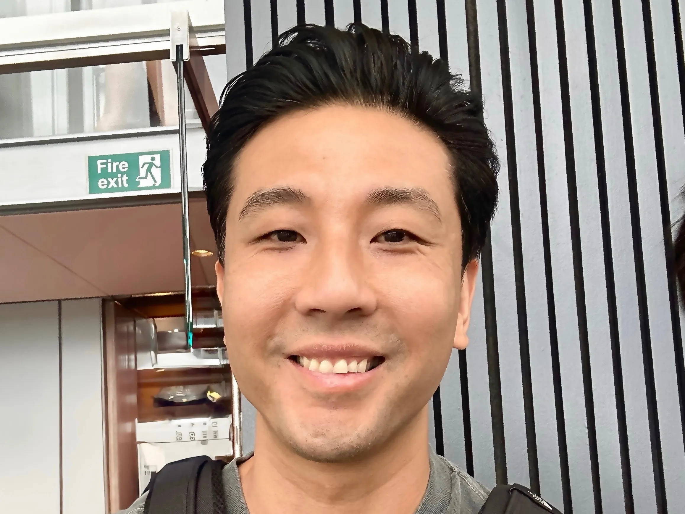 Trung, grinning in front of a wall of dark vertical slats